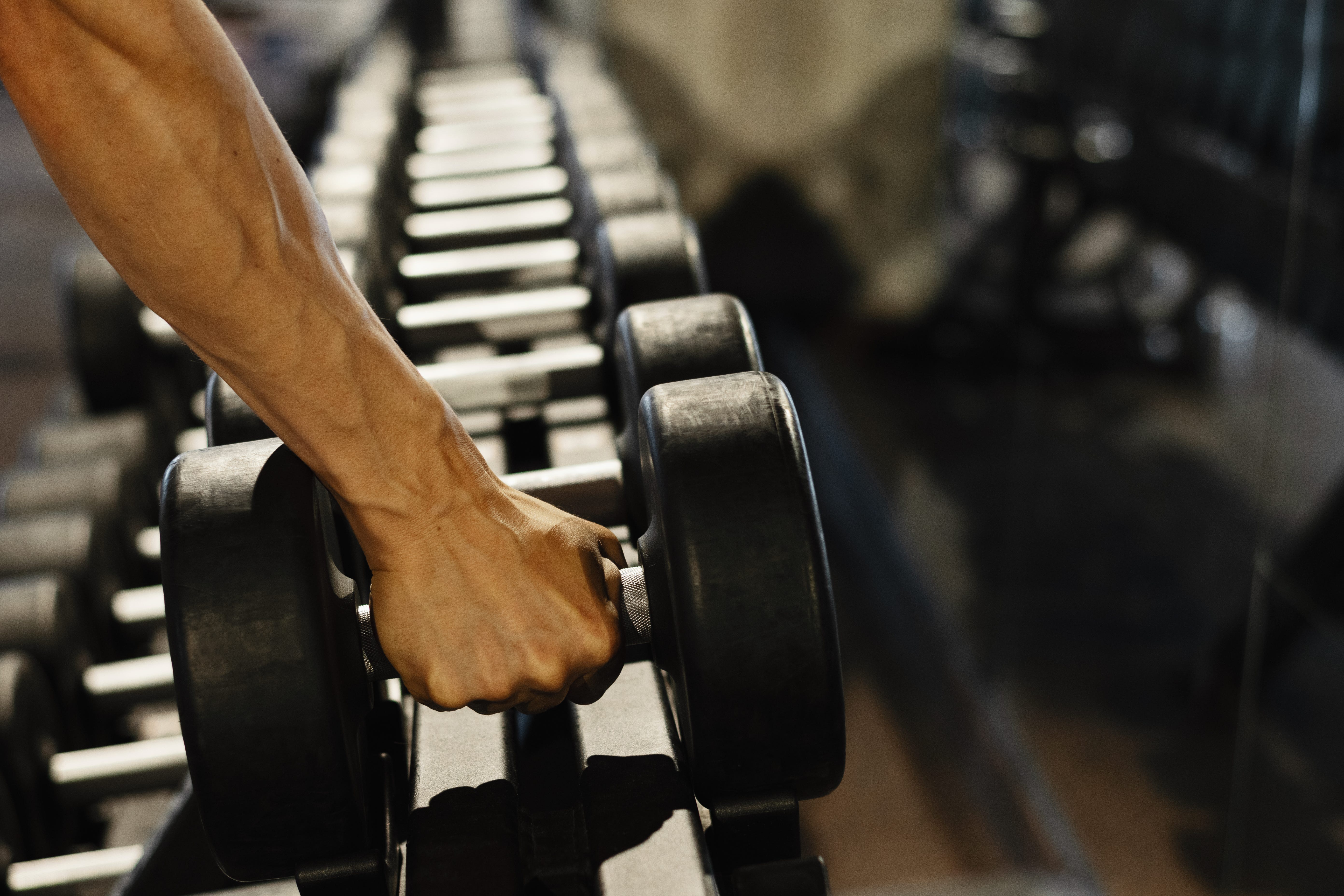 a close-up of a hand grabbing a dumbbell from a rack at the gym.