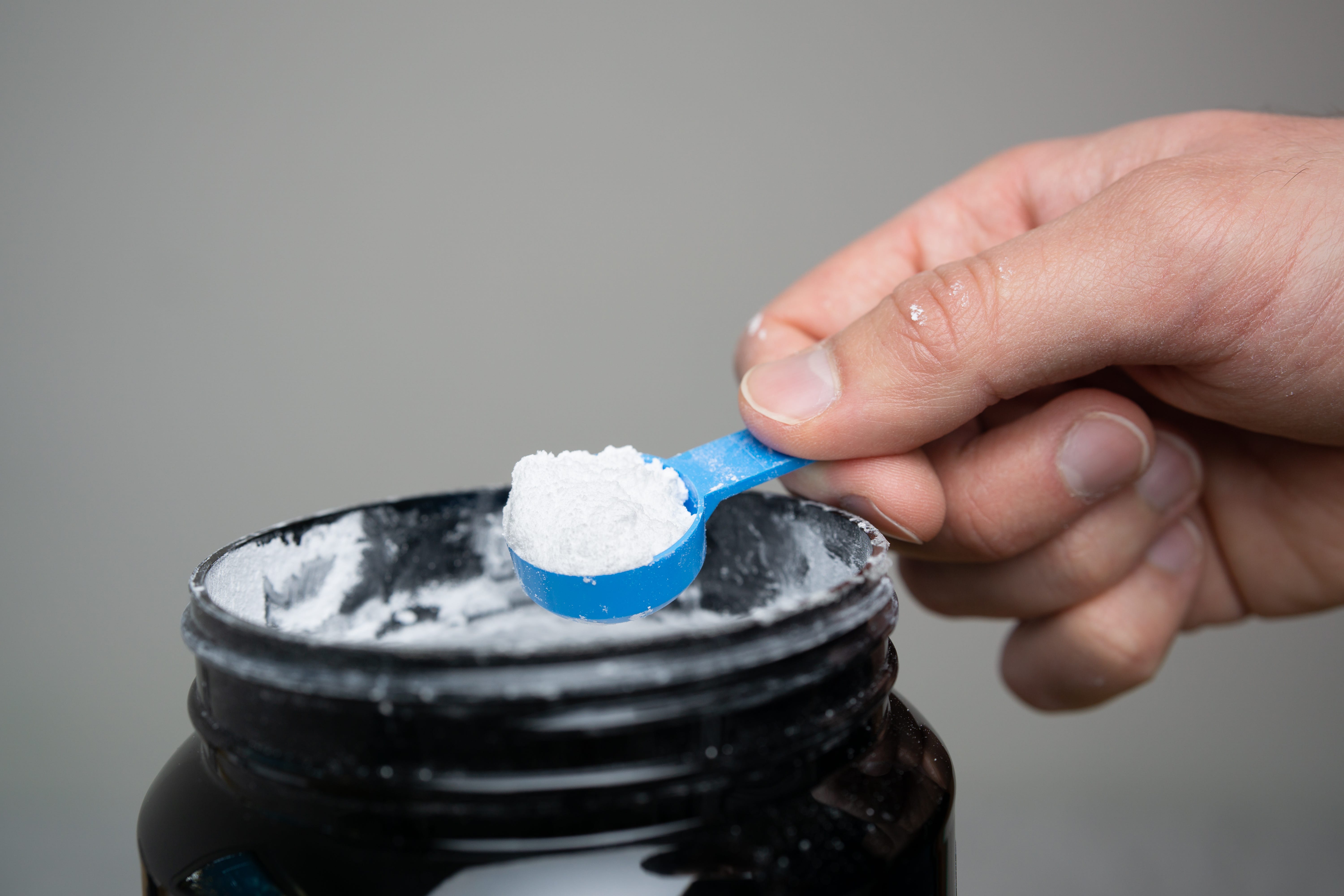 a close-up of a hand lifting a small scoop of white powder supplement from a container.
