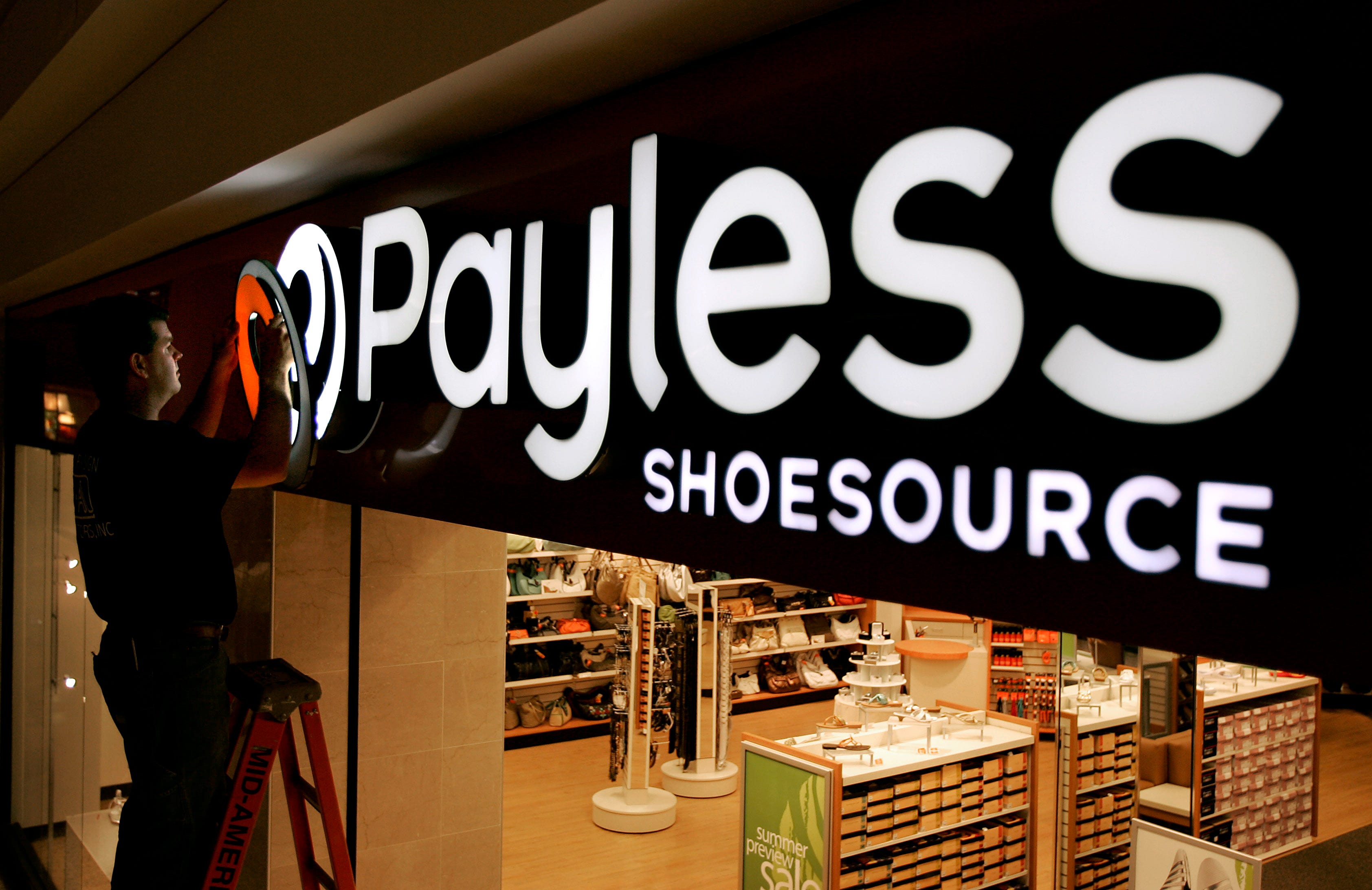 FILE- In this May 18, 2006, file photo a worker puts the finishing touches on a sign unveiling the company's new look at a Payless Shoesource store at a mall in Independence, Mo. Payless ShoeSource has filed for Chapter 11 bankruptcy protection and is shuttering its remaining stores in North America. The filing on Monday, Feb. 18, 2019, came a day after the shoe chain began holding going-out-of-business sales at its North American stores. (AP Photo/Charlie Riedel, File)