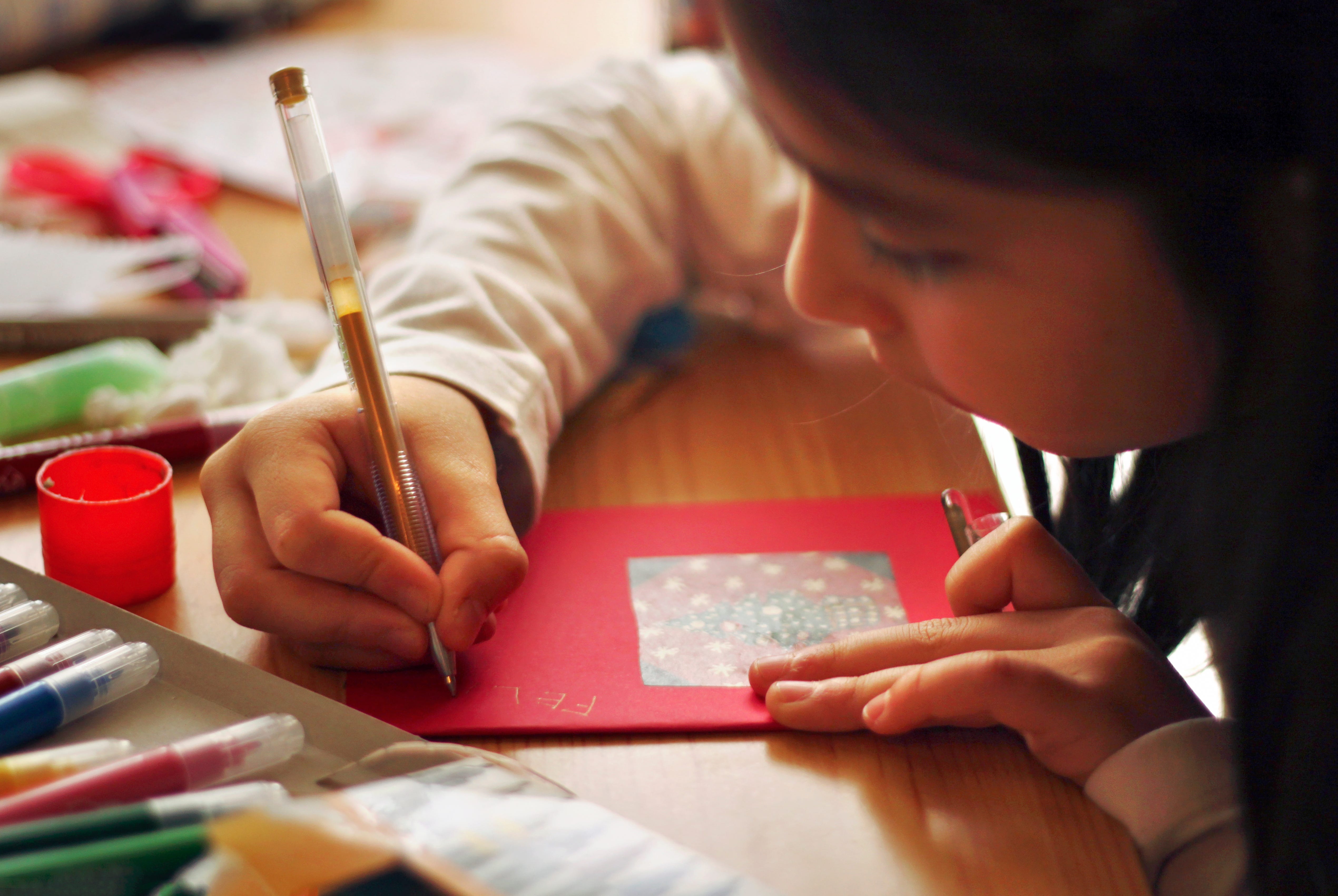 A child writing a thank-you note at a table with colorful pens and markers.