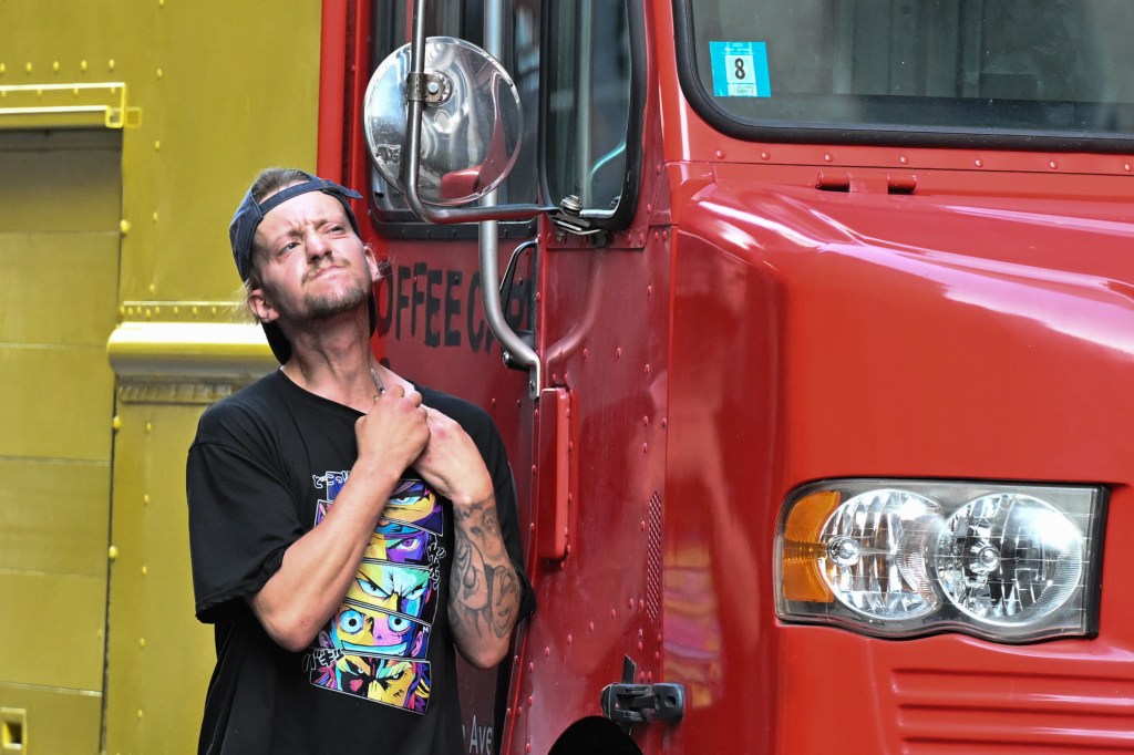 Man with tattoos standing next to a red truck.