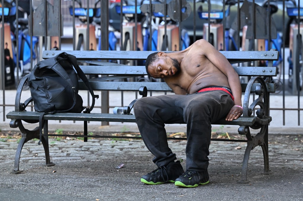 A shirtless man sleeping on a park bench.