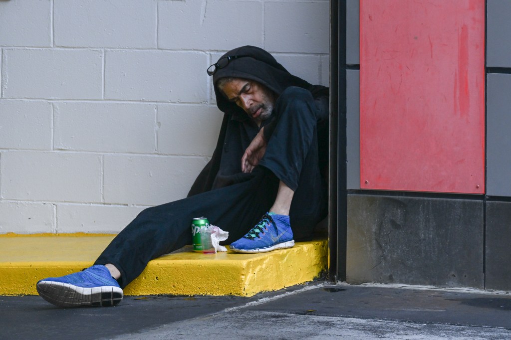 Man sleeping against a wall with a soda can beside him.