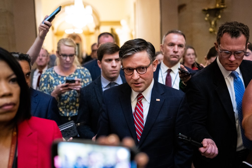 A man in a suit walks through a crowd of people holding phones.