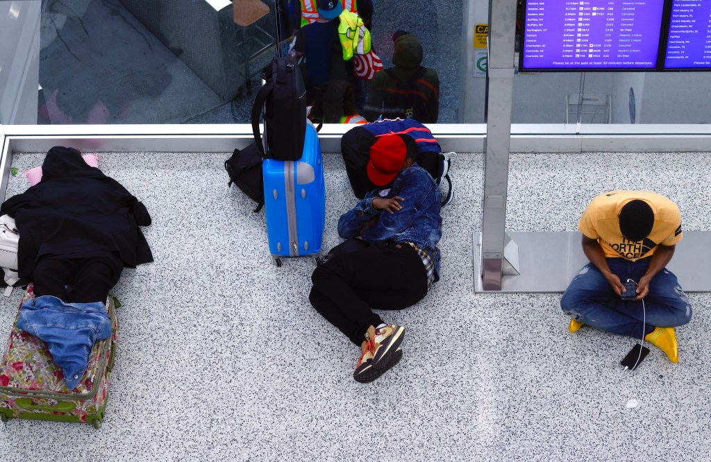Passengers sleeping and using phones in a Newark airport terminal due to flight cancellations.