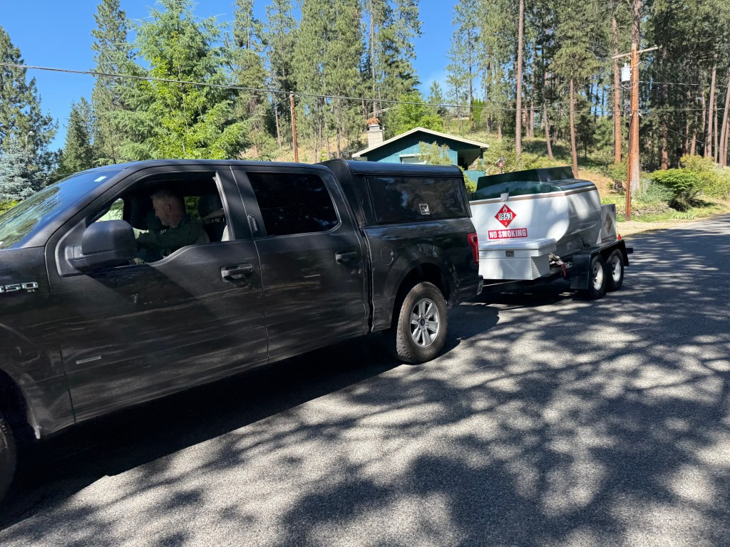 A dark-colored pickup truck towing a fuel tanker on a road.