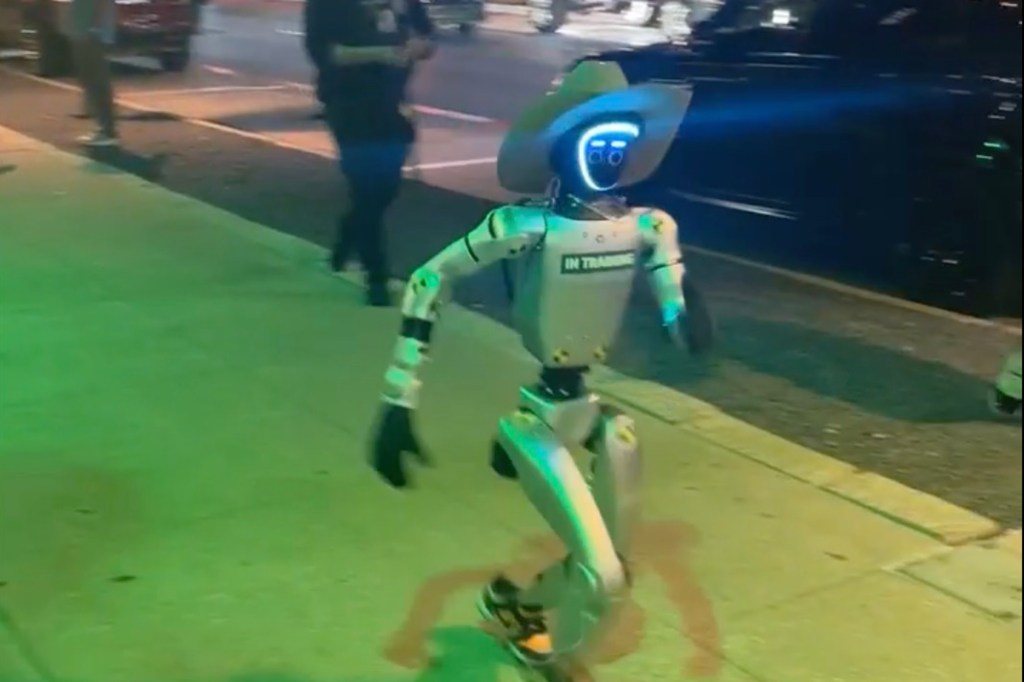 Robot wearing a cowboy hat walks down a city street.