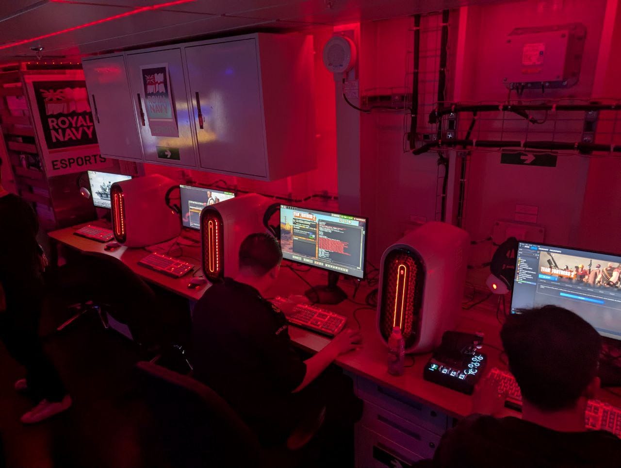 A Royal Navy sailor sits at one of four gaming computers in a row.