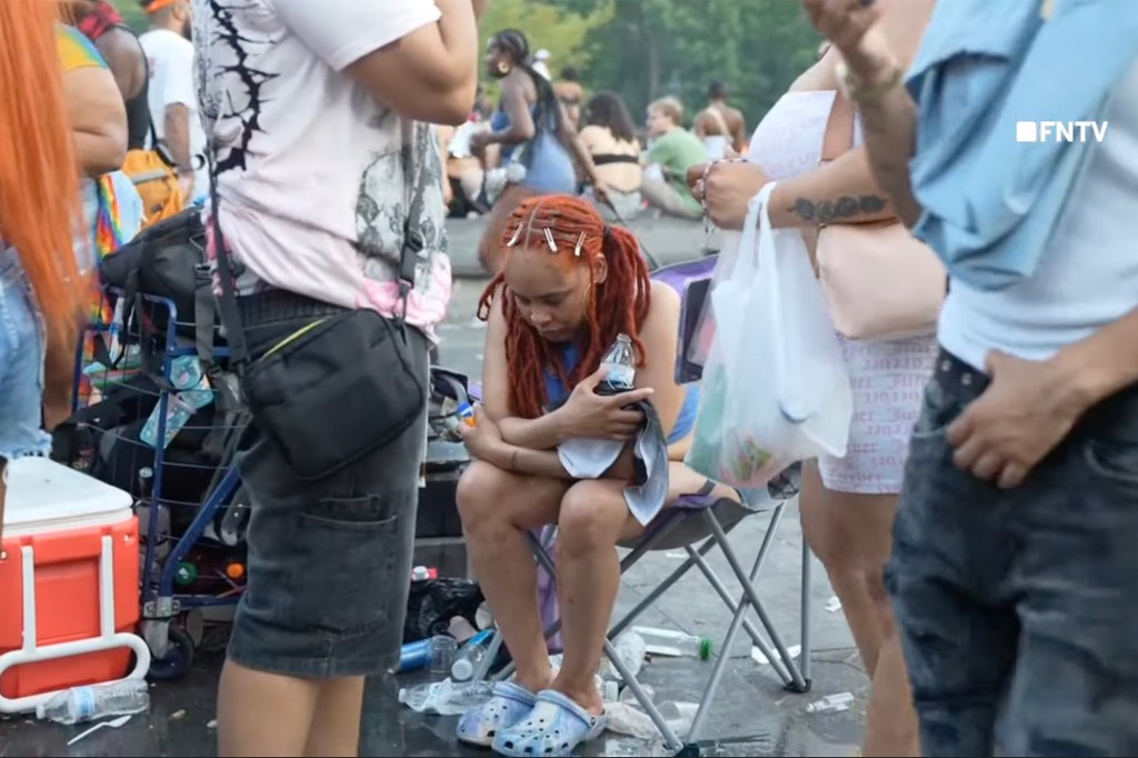 Woman sitting on a chair in a crowded outdoor setting.