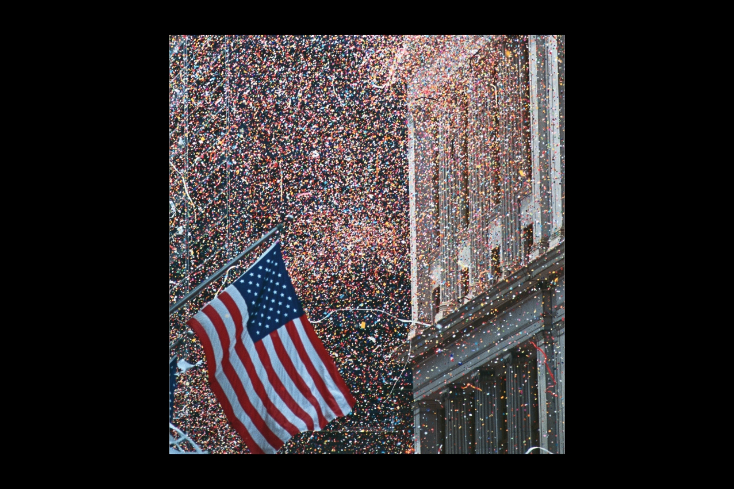 An image of a U.S. flag in front of a NYC ticker tape parade inset on a black background.