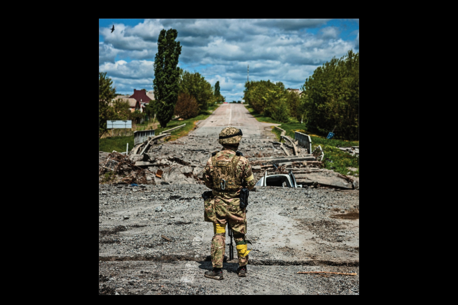 A soldier is seen from behind in combat gear on a broken war-torn road.