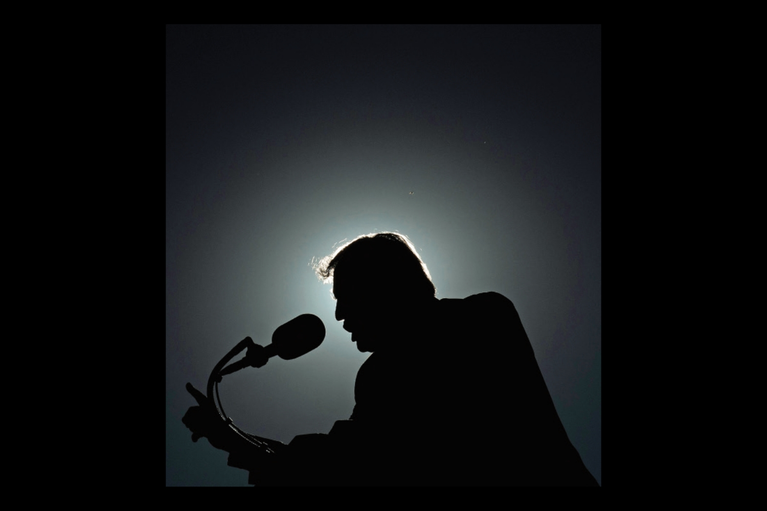 An image of Donald Trump silhouetted against a halo of light as he speaks into a microphone. The photo is inset on a black background.