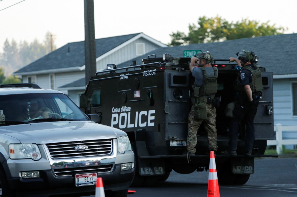 Police officers in tactical gear near an armored vehicle.