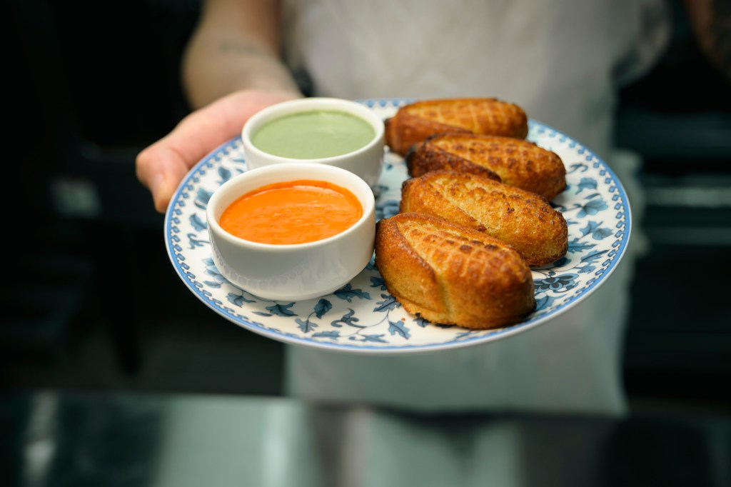 Green and red hot sauces are shown with a side of corn bread at Hudson VU.
