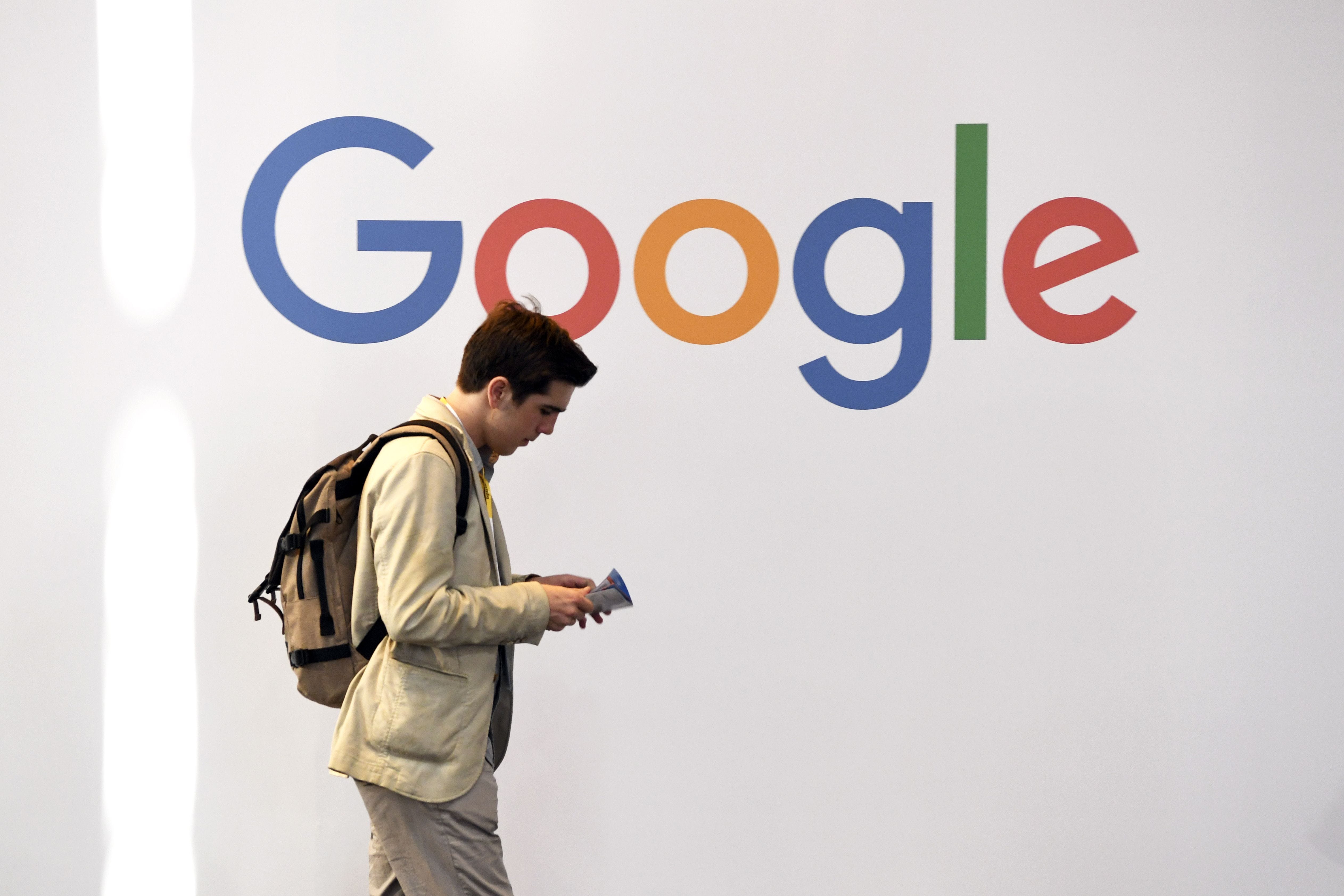 A man reading a pamphlet walks past a wall displaying the Google logo.
