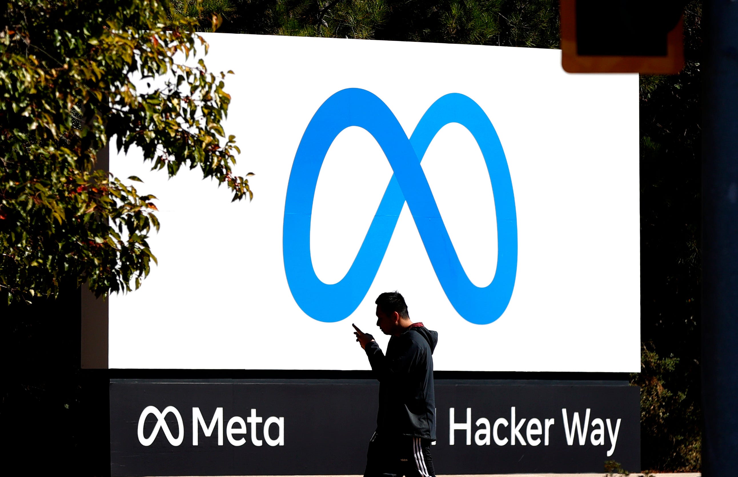 A man walking past Meta's company logo in front of their headquarters in Menlo Park, California.