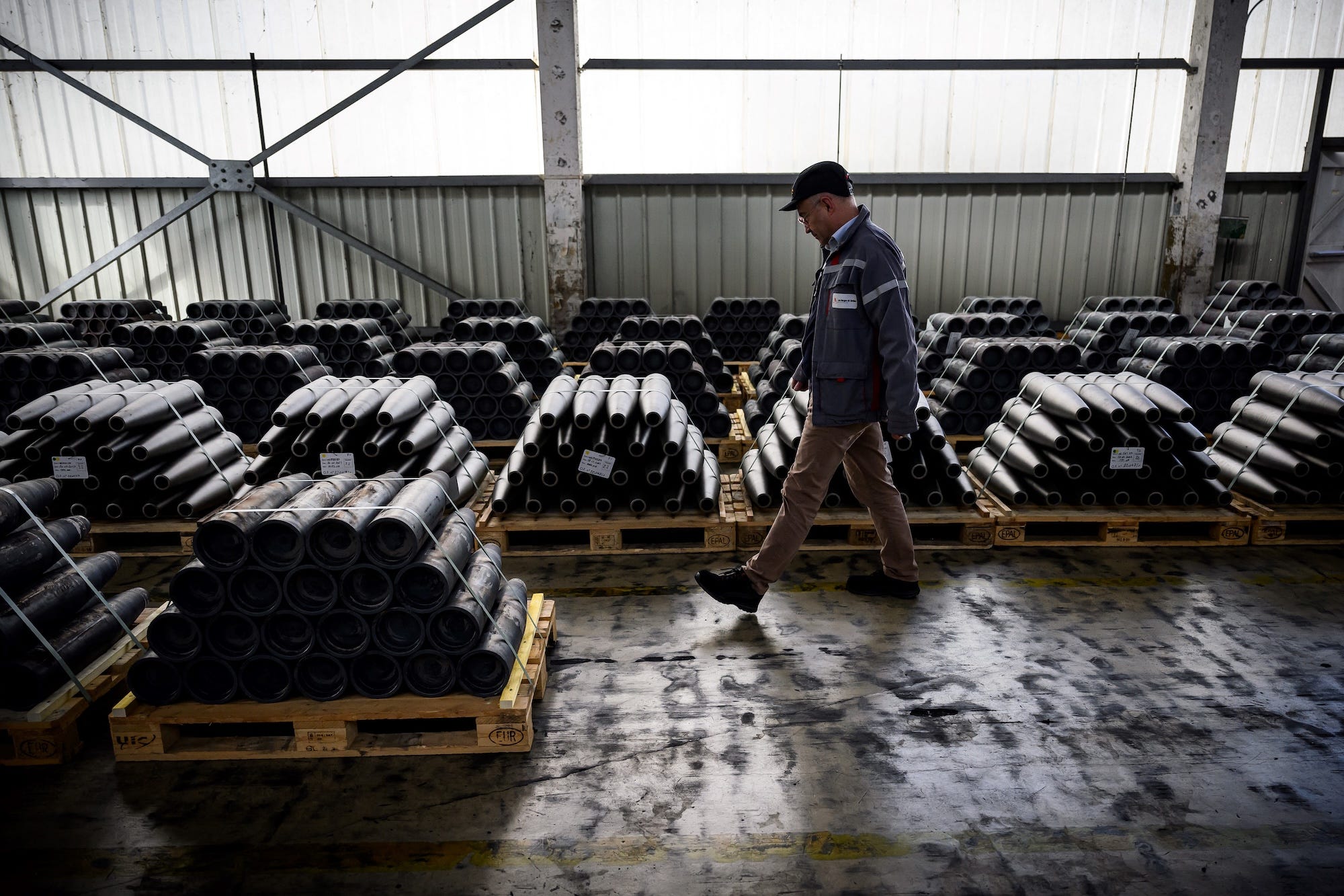 A man walks past piles of 155mm shells on wooden pallets