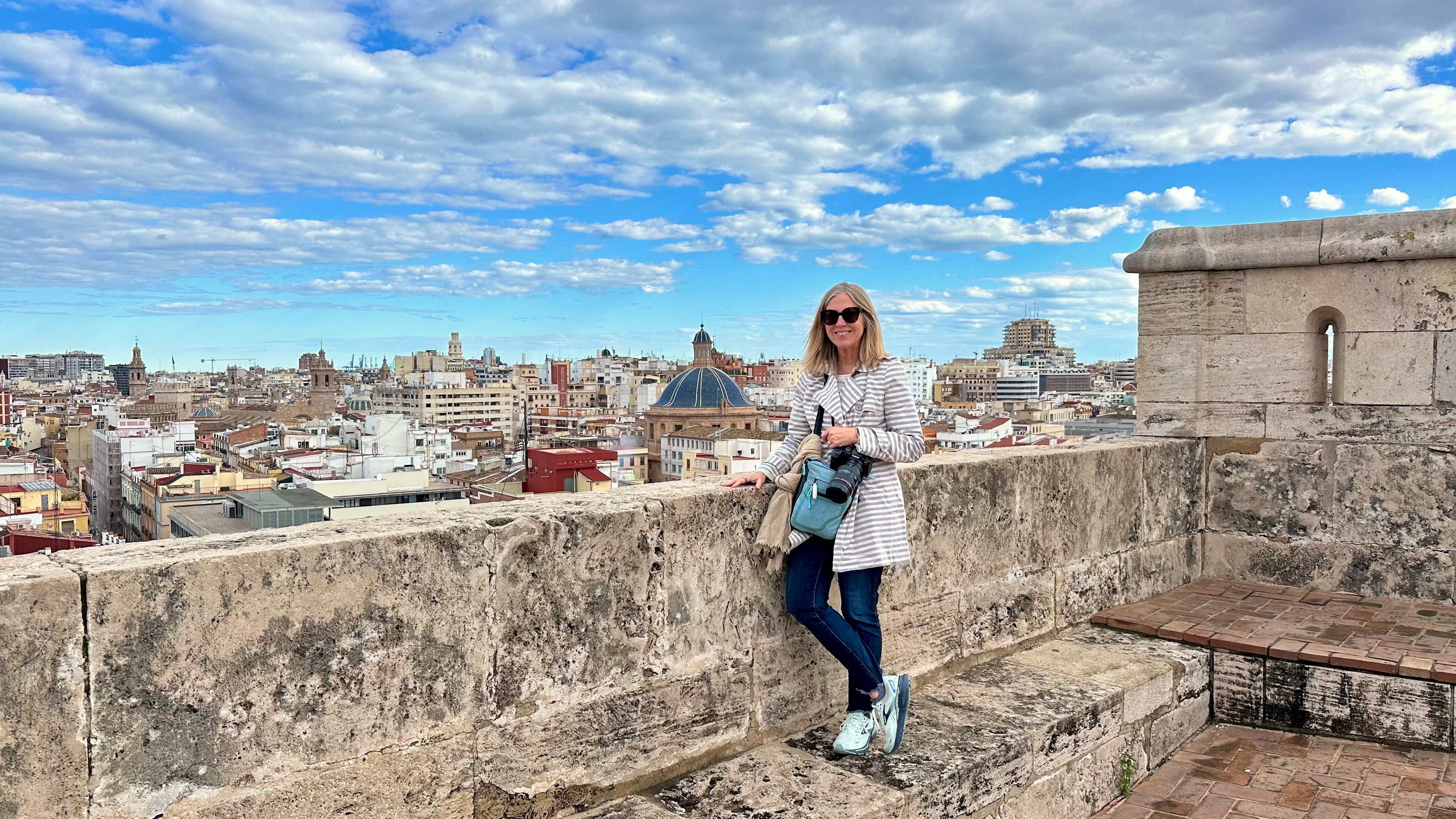 Author Lisa VanderVeen smiling next to ledge of building overlooking aerial view of a city, clouds in Valencia, Spain