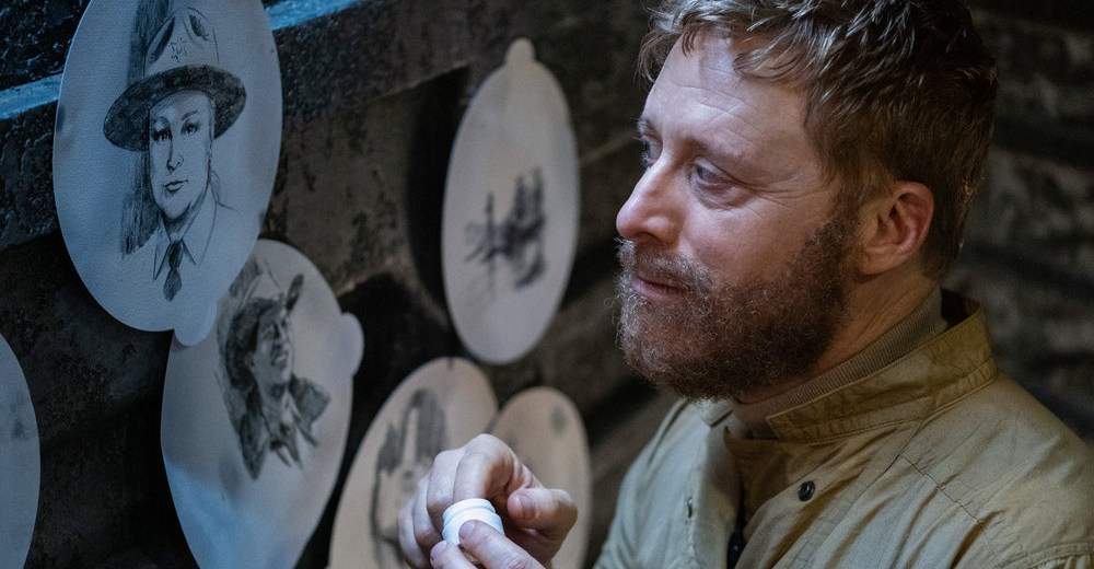 Harry (Alan Tudyk) looks sadly at sketches of Elizabeth Bowen’s Deputy Liv Baker and Corey Reynolds’ Sheriff Mike Thompson in season 4 of Resident Alien