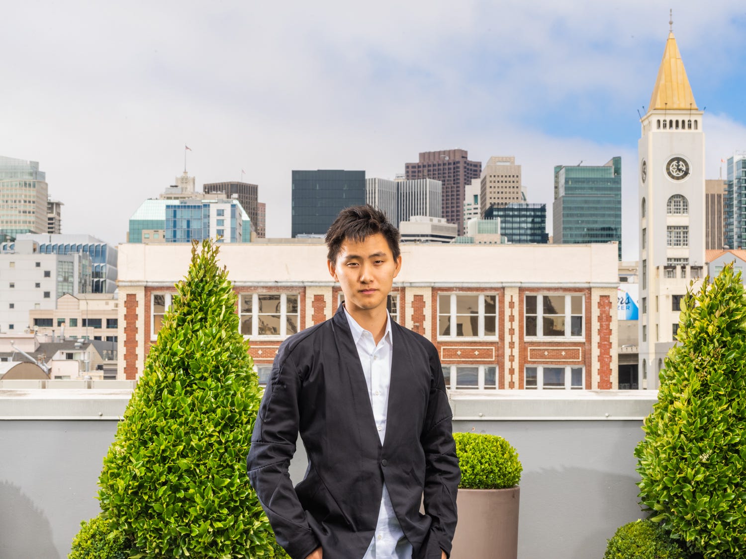 Scale AI cofounder and CEO Alexandr Wang poses for a photo on a rooftop with a cityscape behind him.