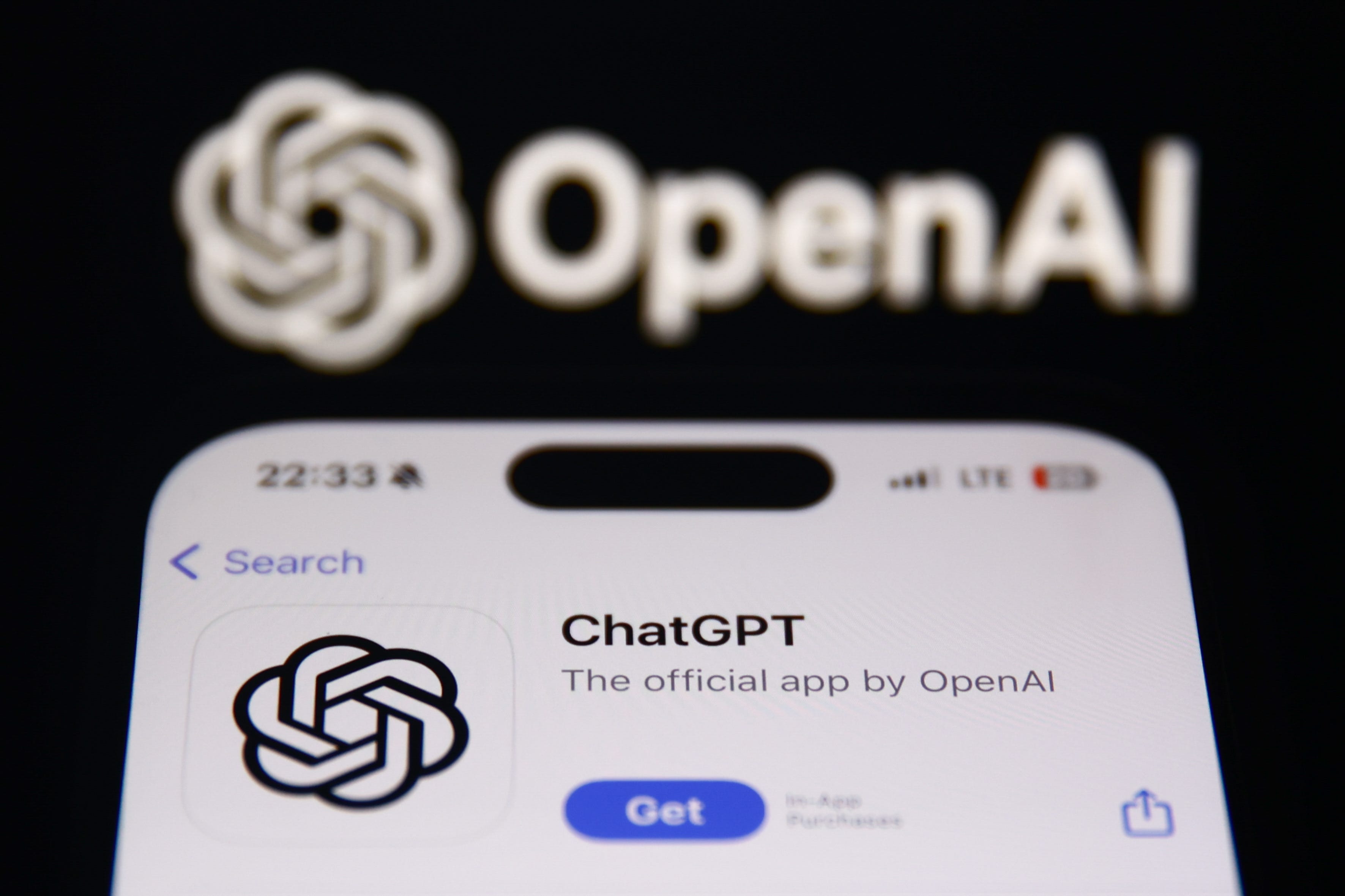 The ChatGPT page on Apple's App Store being displayed on a phone screen in front of the OpenAI logo.