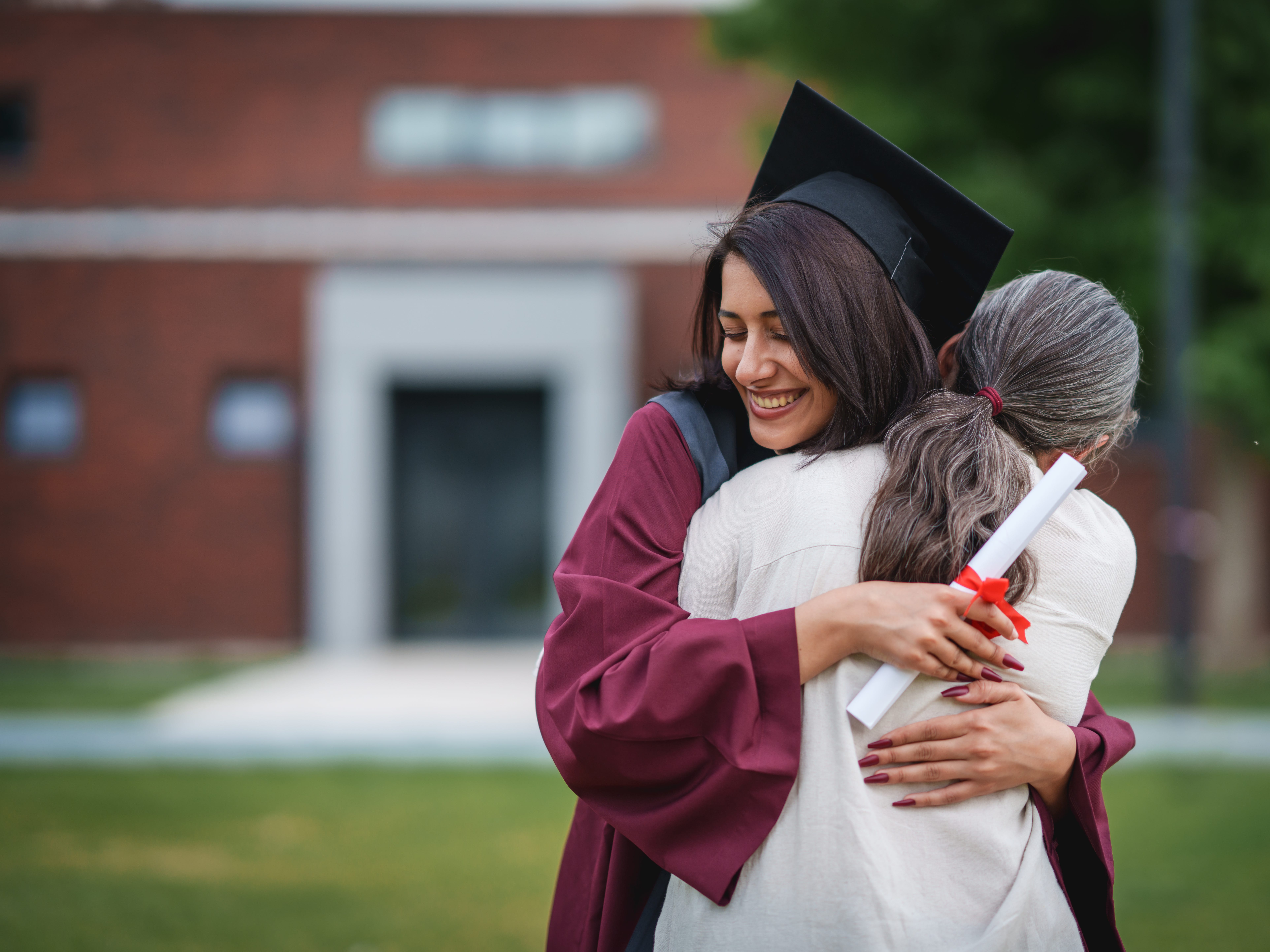 a mother hugging her daughter dressing in graduation gown