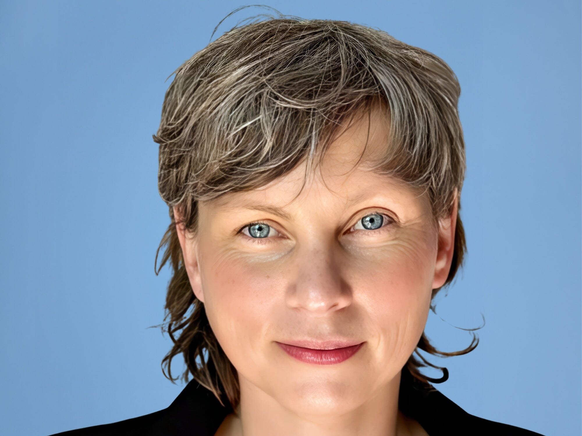 Sarah Rich is photographed against a blue background and wears a black collared shirt.