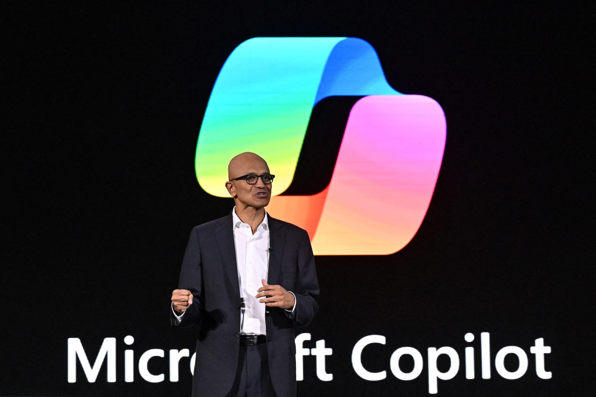 Microsoft CEO Satya Nadella speaks in front of a large screen displaying the words "Microsoft Copilot."