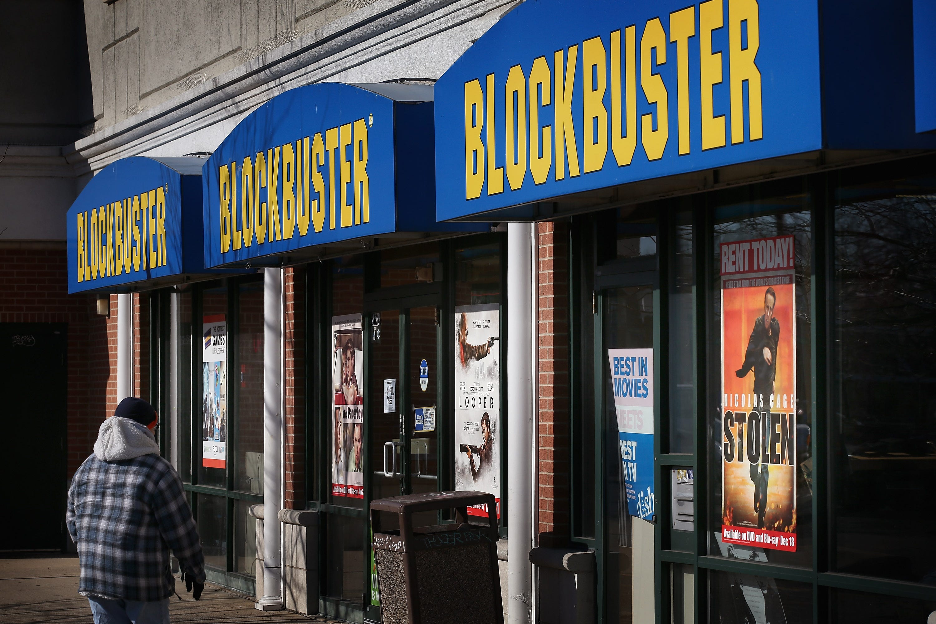 A man walks in front of a Blockbuster video store.