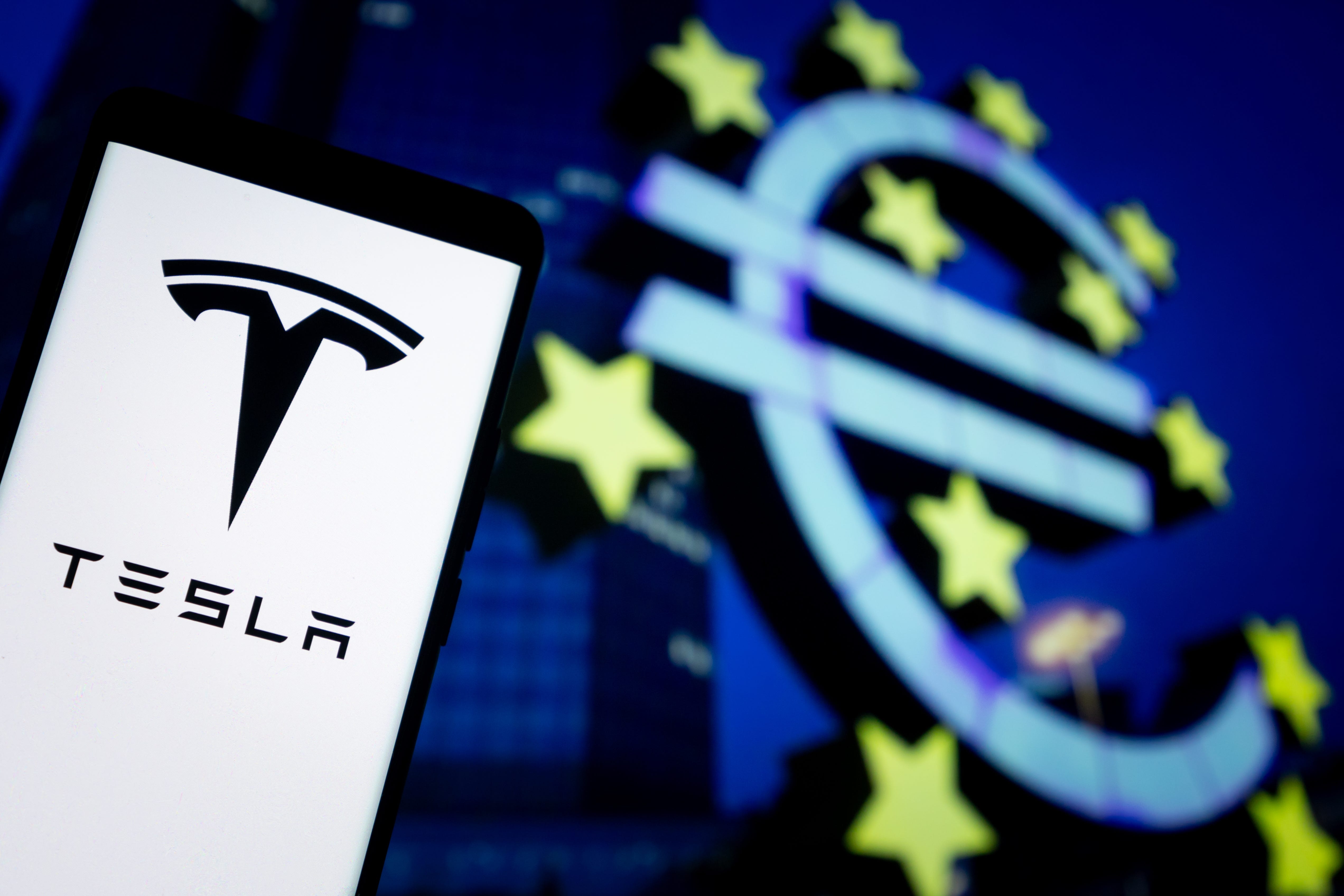 The logo of Tesla is displayed on a smartphone screen with an EU flag in the background in Chongqing, China, on June 25, 2025