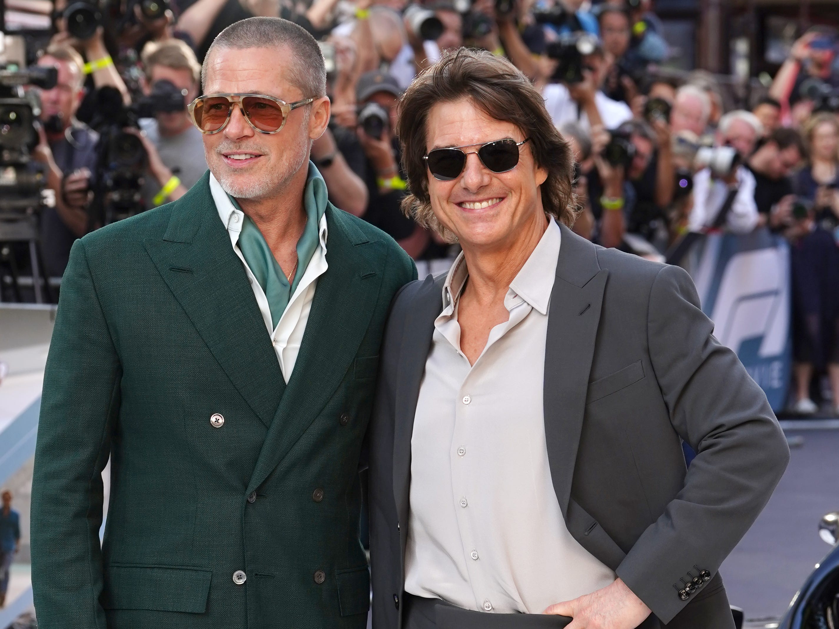 Brad Pitt in a green suit and Tom Cruise in a grey suit posing for a picture together at a premiere.