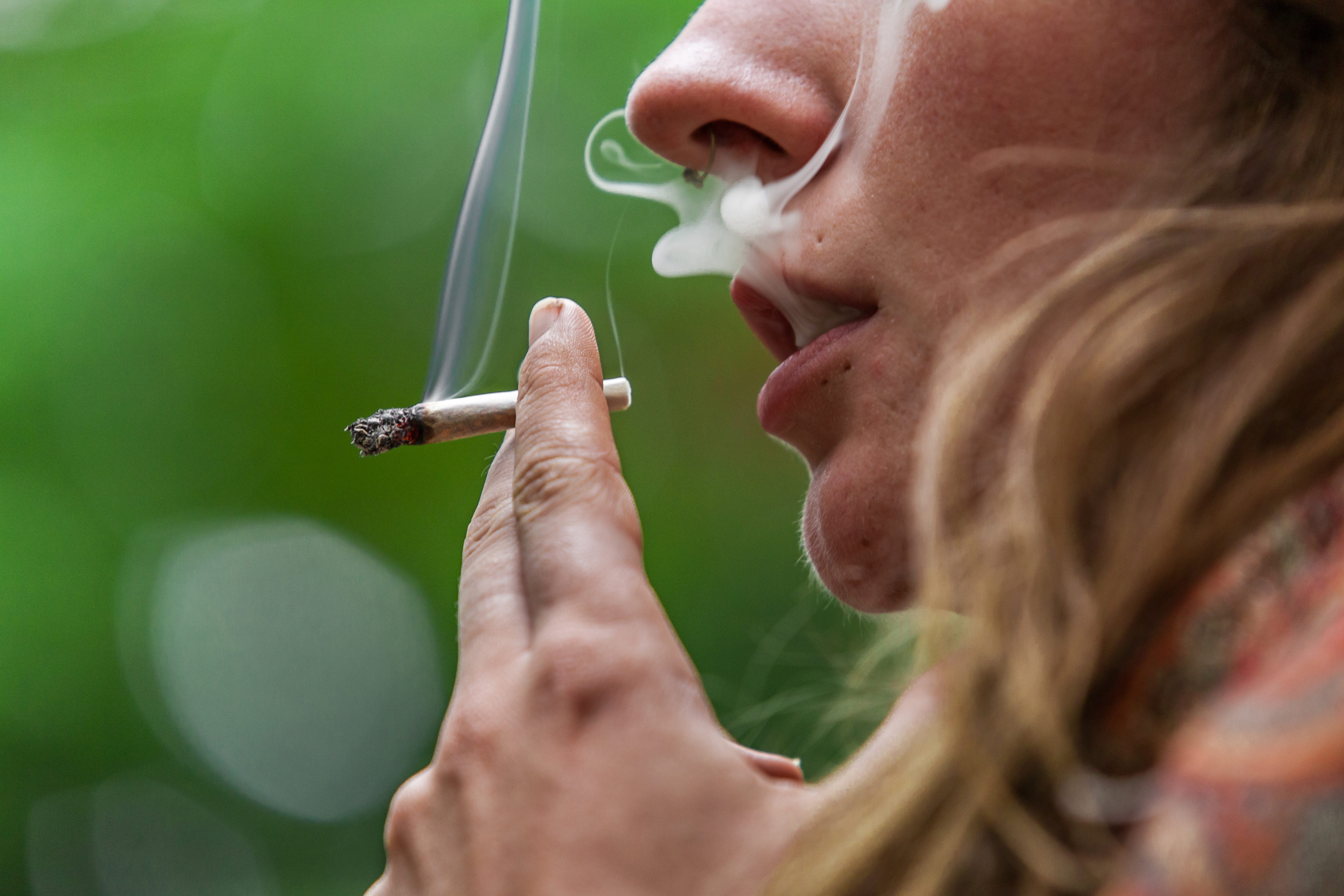 A close-up of a young woman smoking marijuana outdoors
