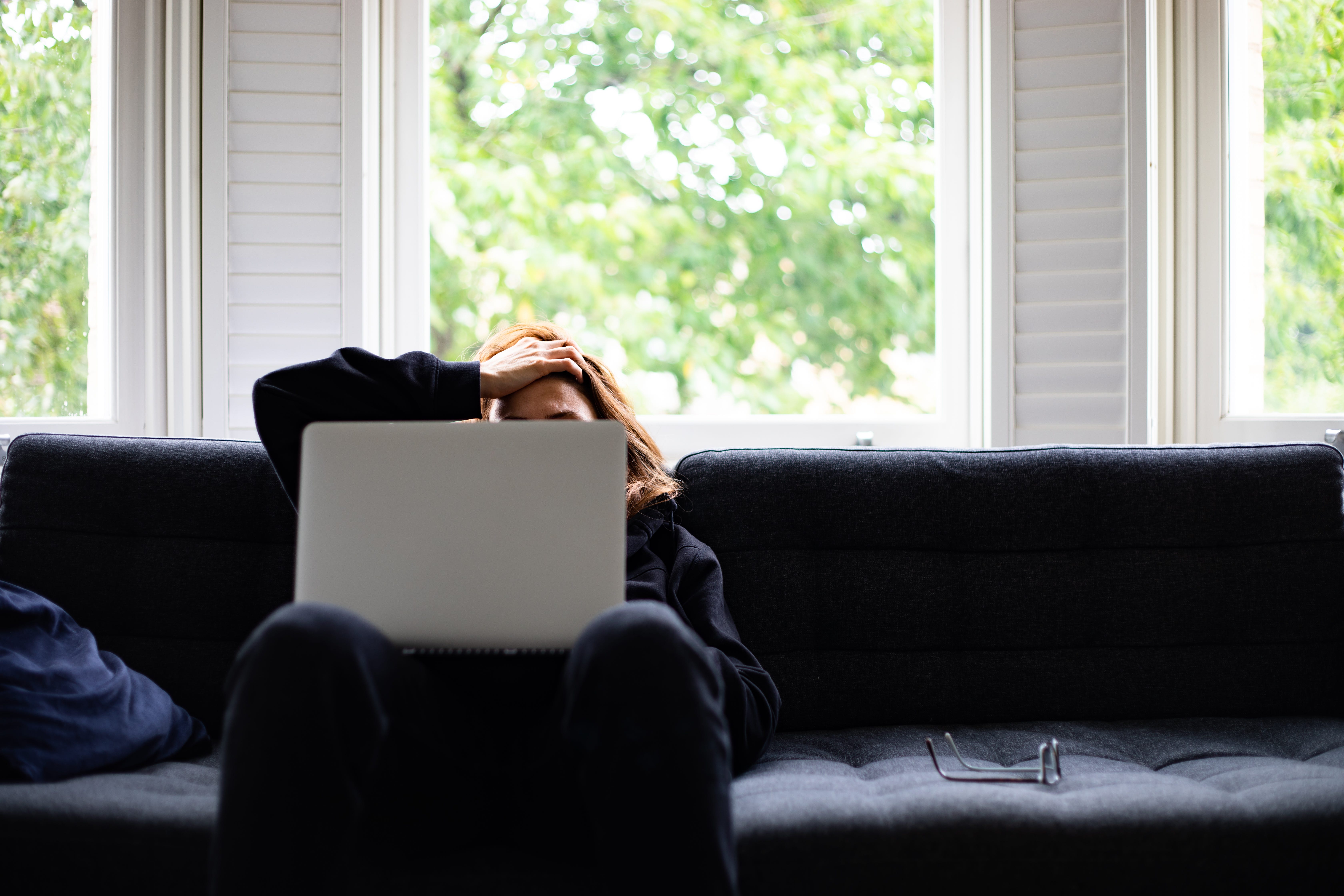 A woman sitting in a couch looks distressed at her computer.