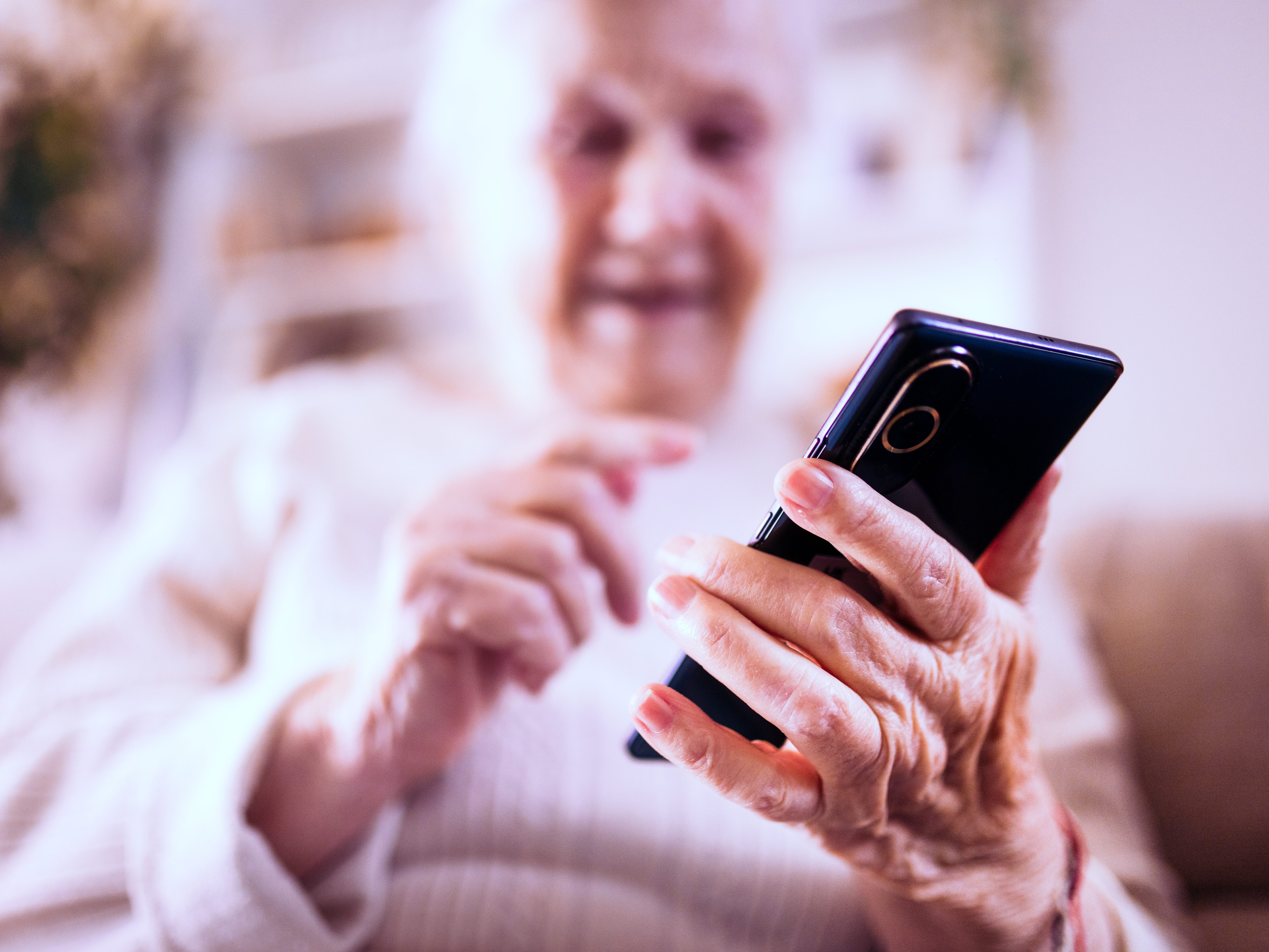 Grandmother at home sitting at the table and using smart phone.