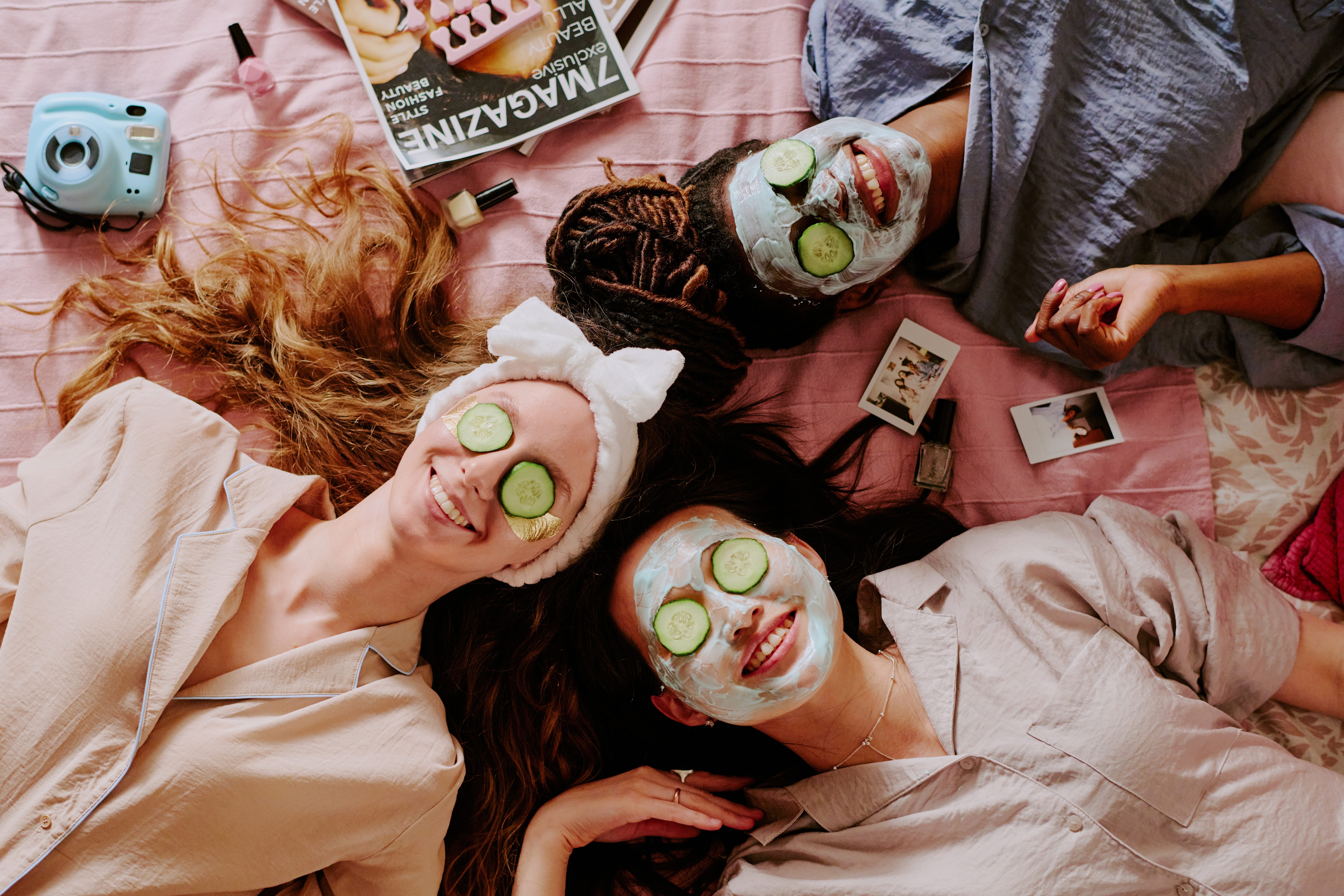 Three teen girls wearing face masks and cucumbers over their eyes smile while at a sleepover.