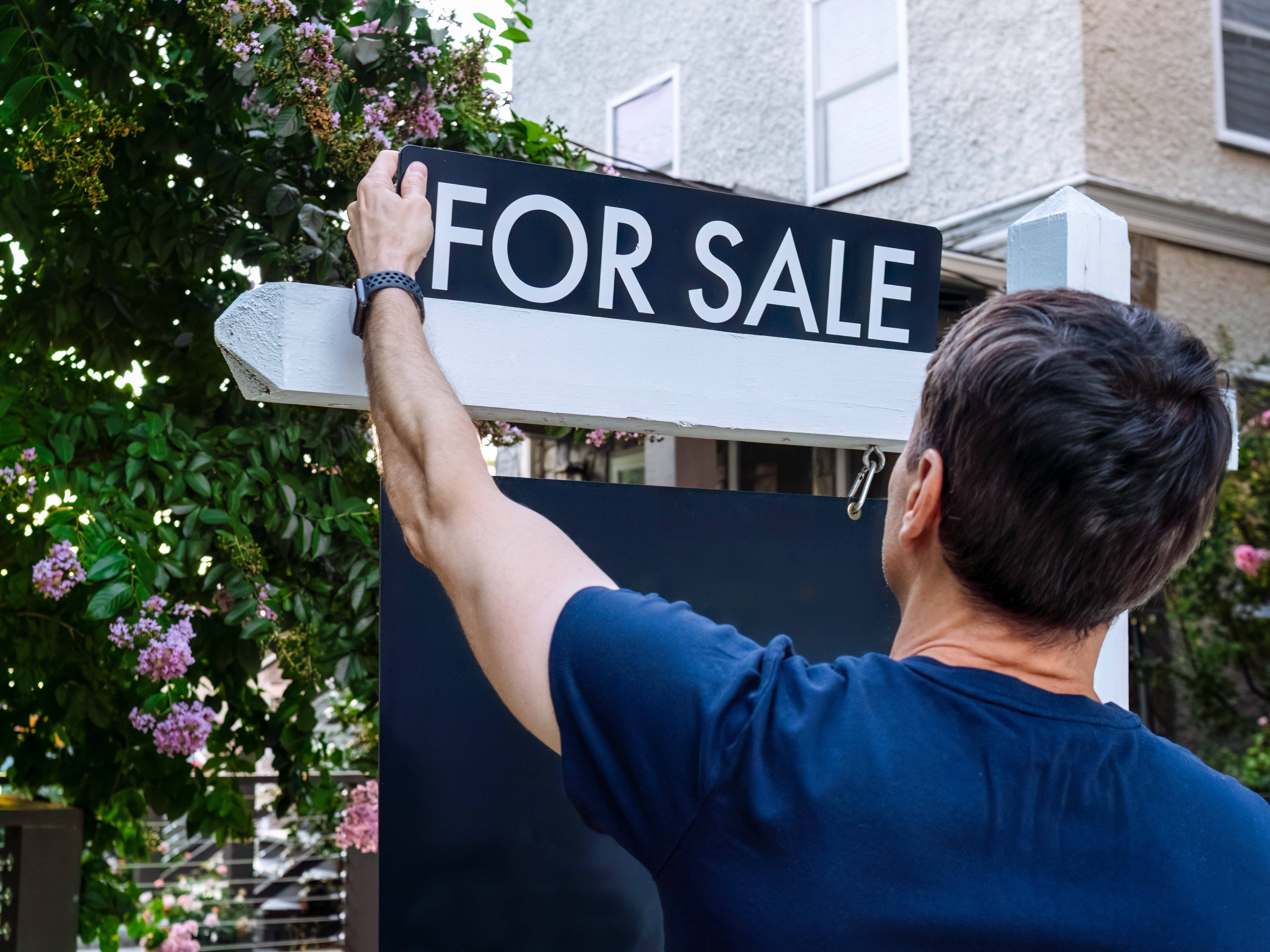 a man putting a "for sale" sign up on his lawn