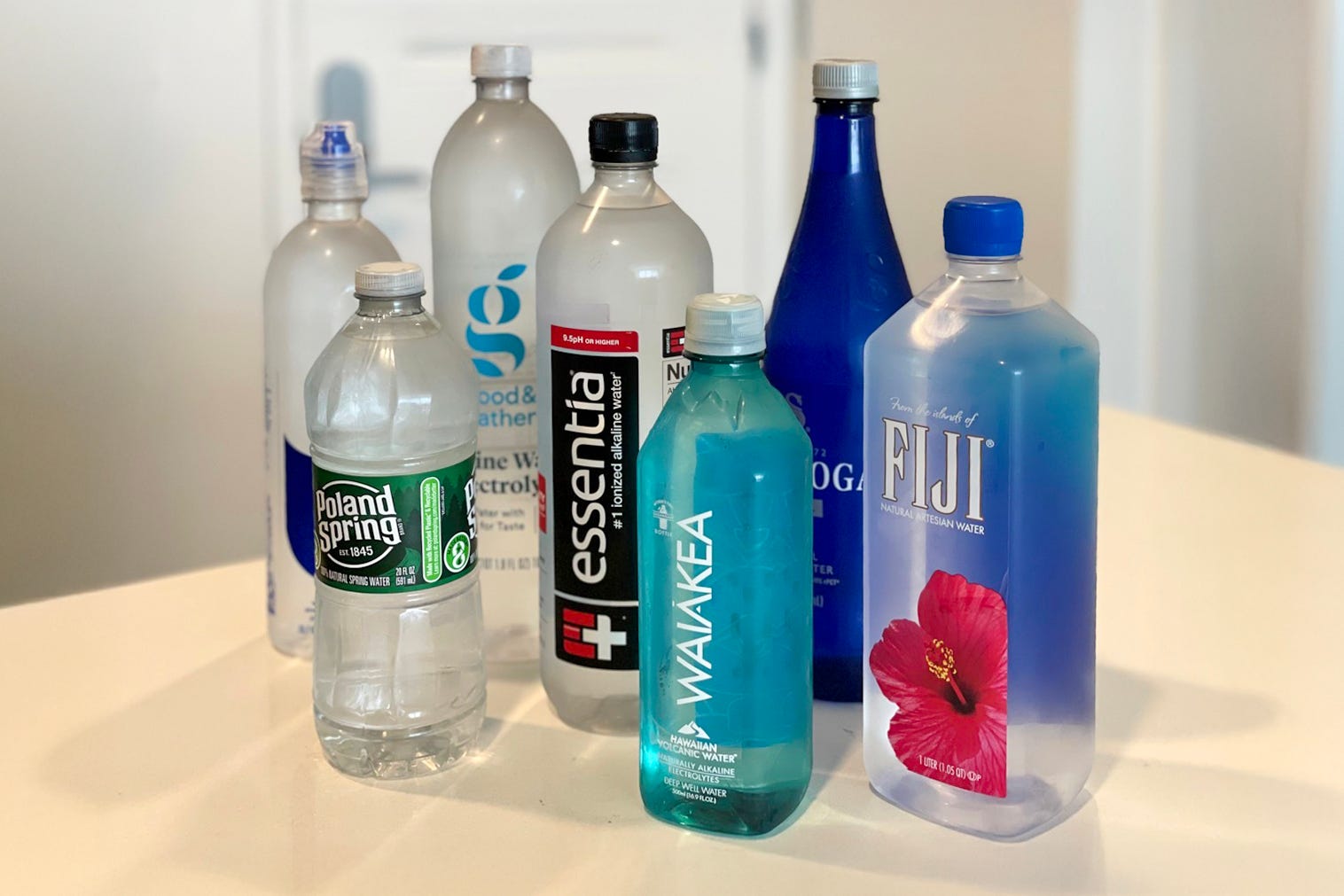 Group of water bottles from Poland Spring, Waiakea, Fiji, Saratoga, Essentia, Good and Gather, Smartwater on counter
