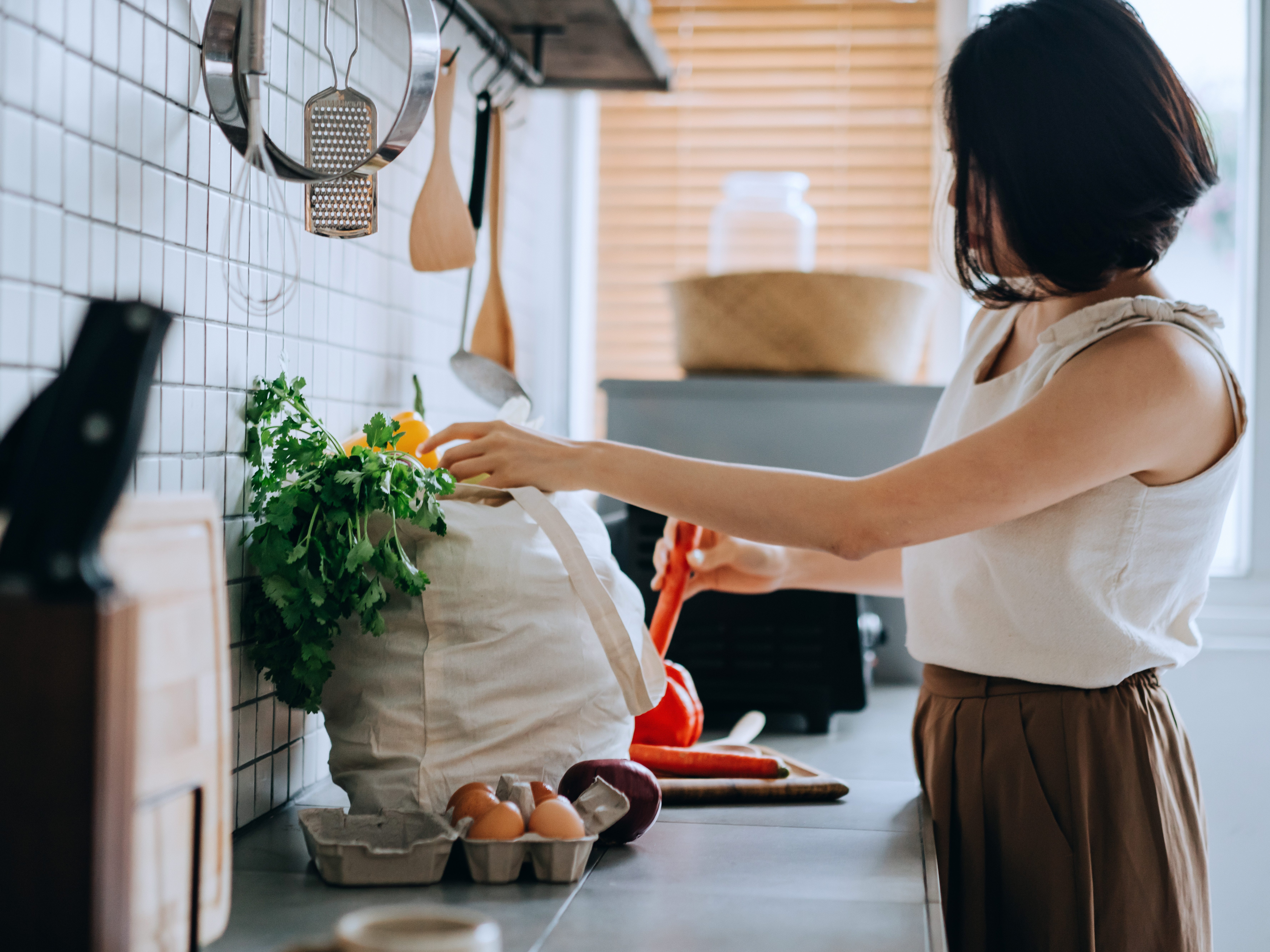 A woman standing at a counter unloading a bag of groceries onto the counter.