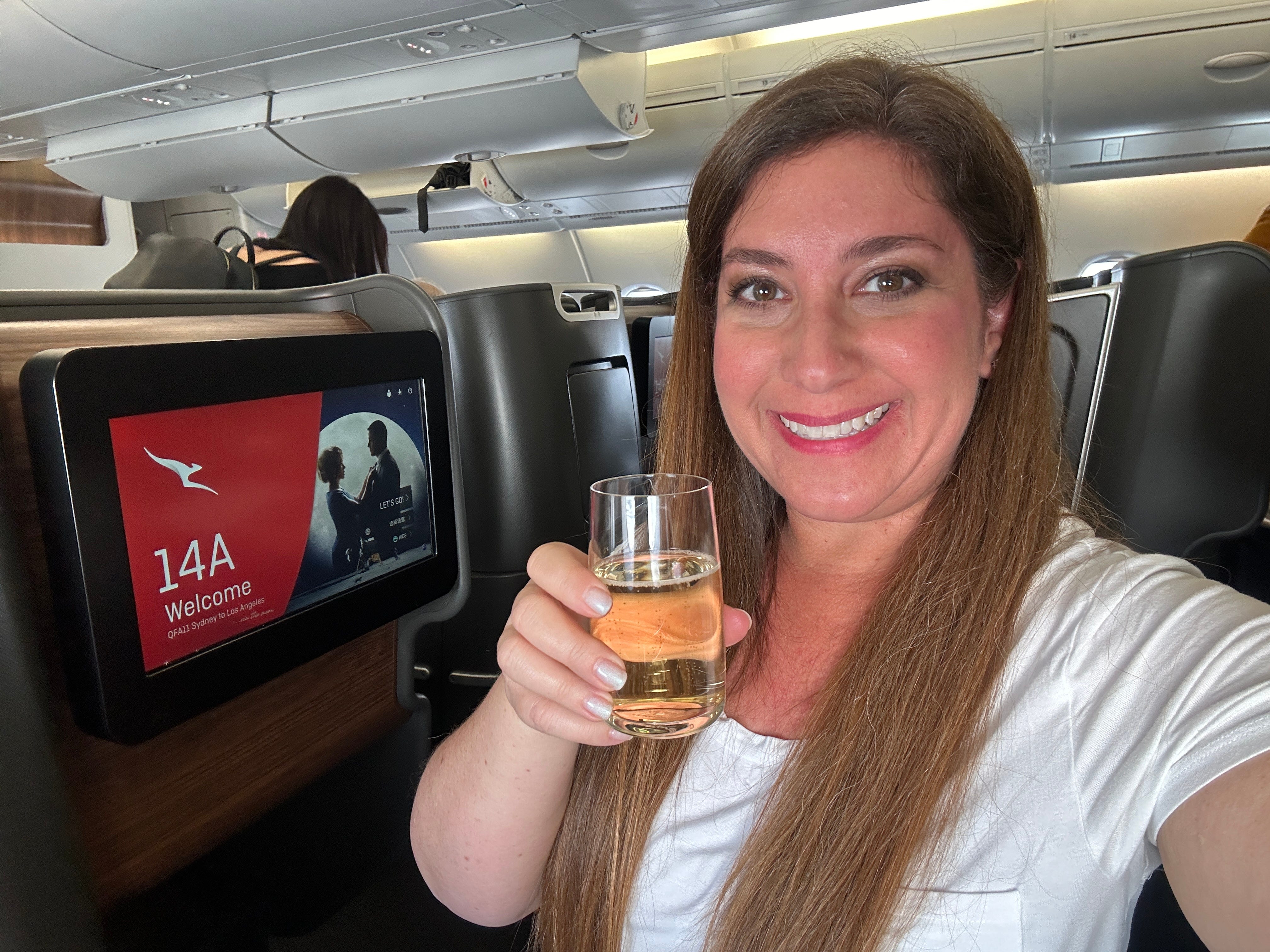 Author Jill Schildhouse smiling with alcohol glass on Qantas flight