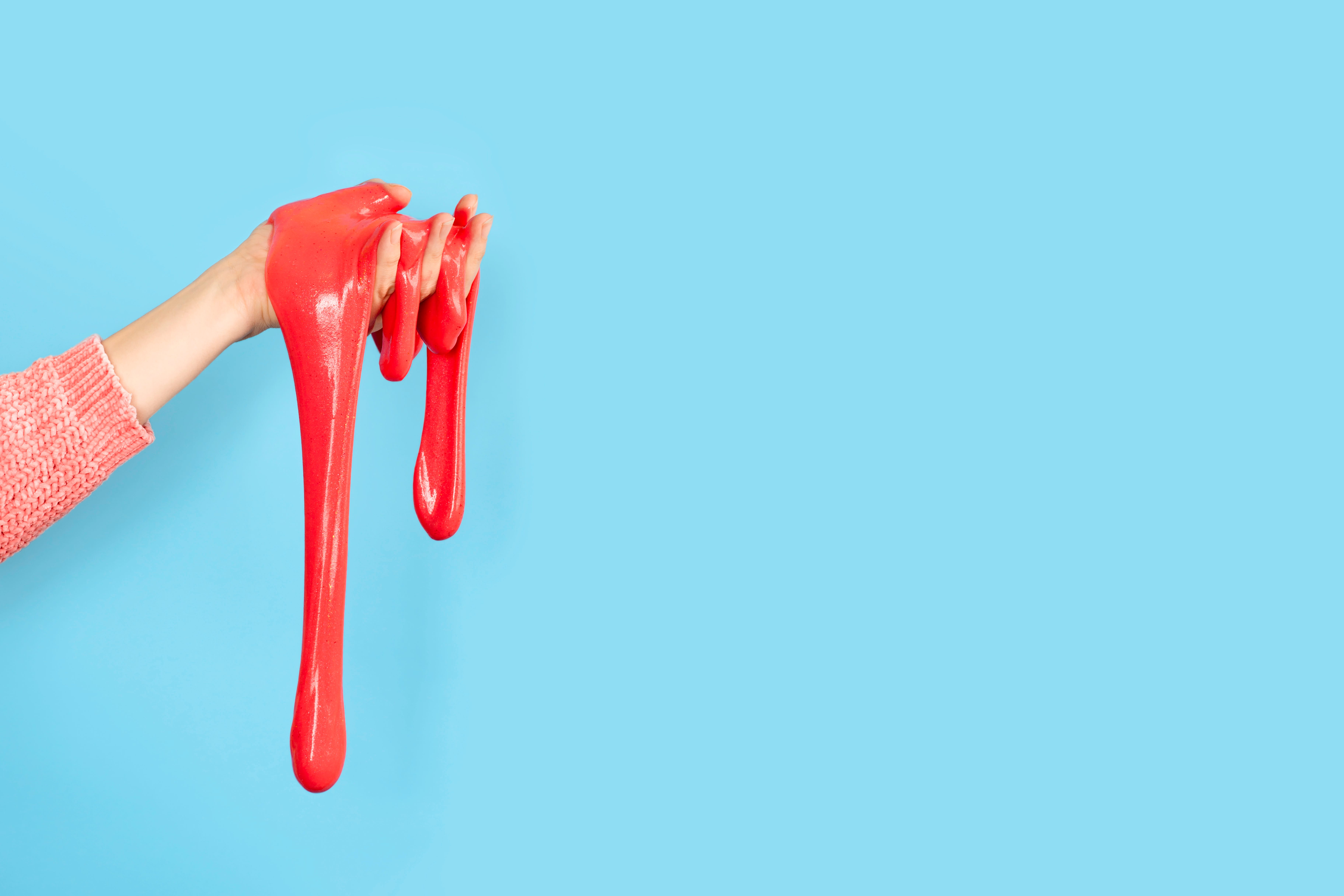 Close up on shiny Red or coral slime in the hand isolated on blue background