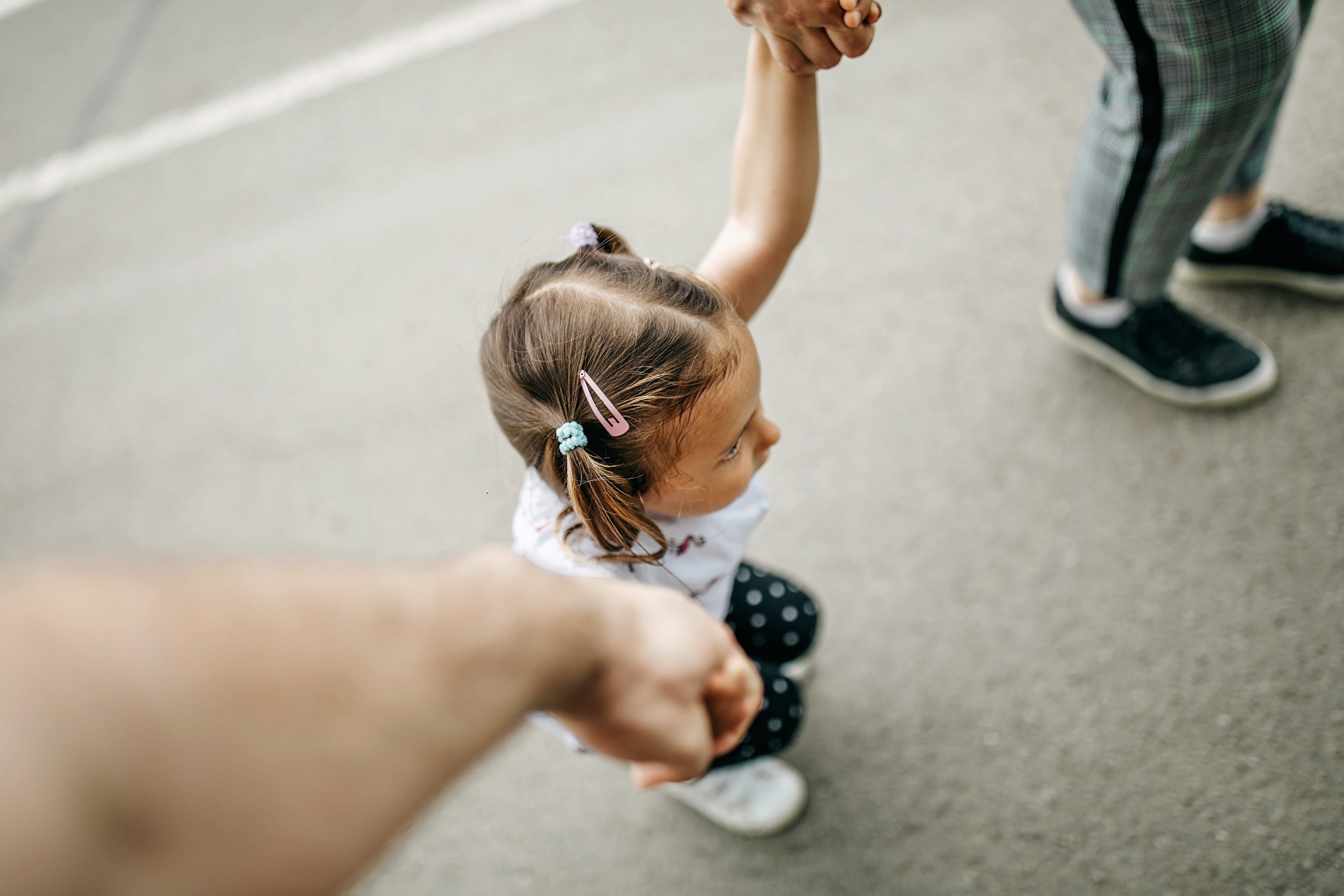 A little girl holds her parents hands.