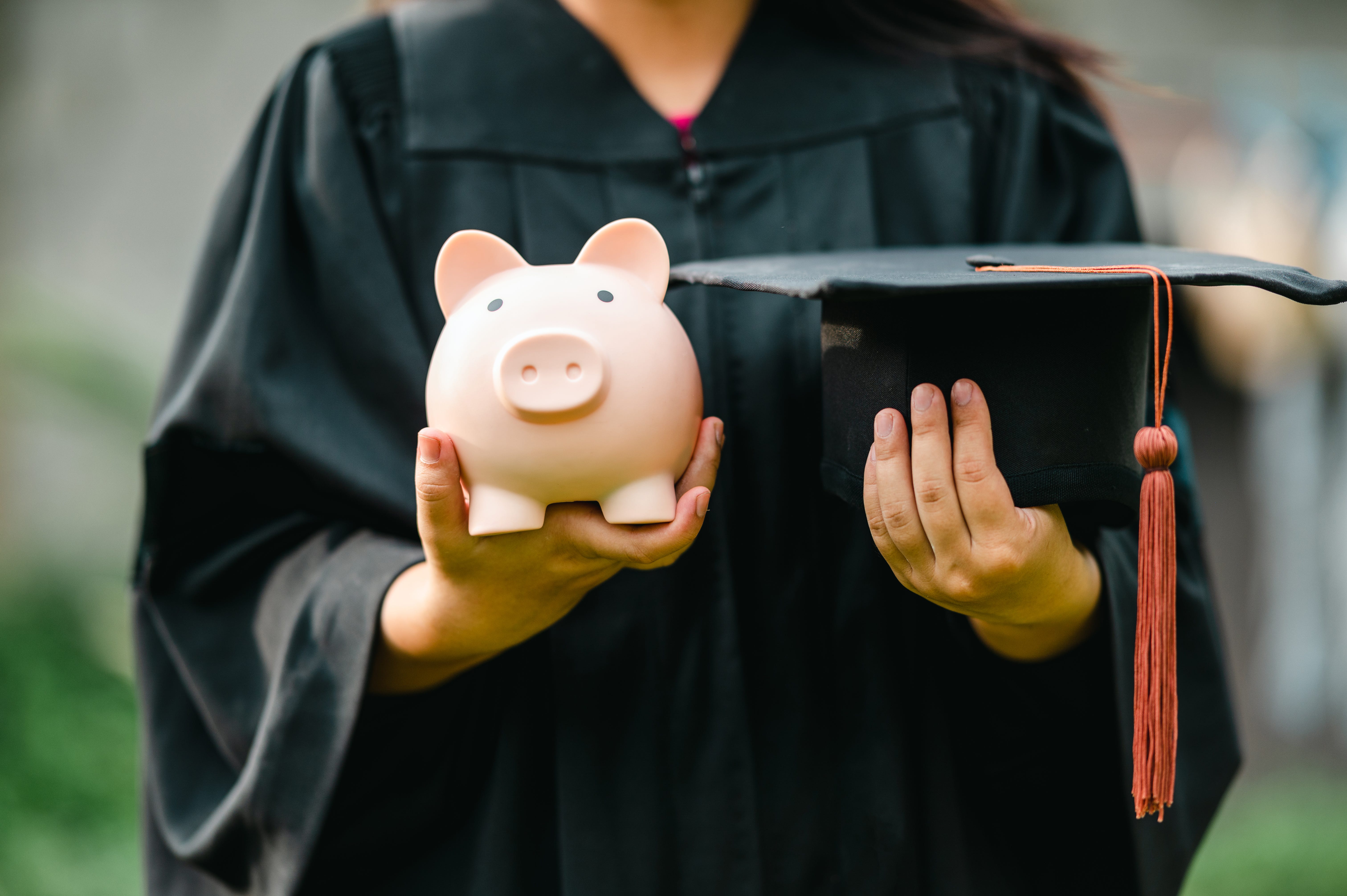 A college student holds a piggy bank on her left hand and a cap on her right.