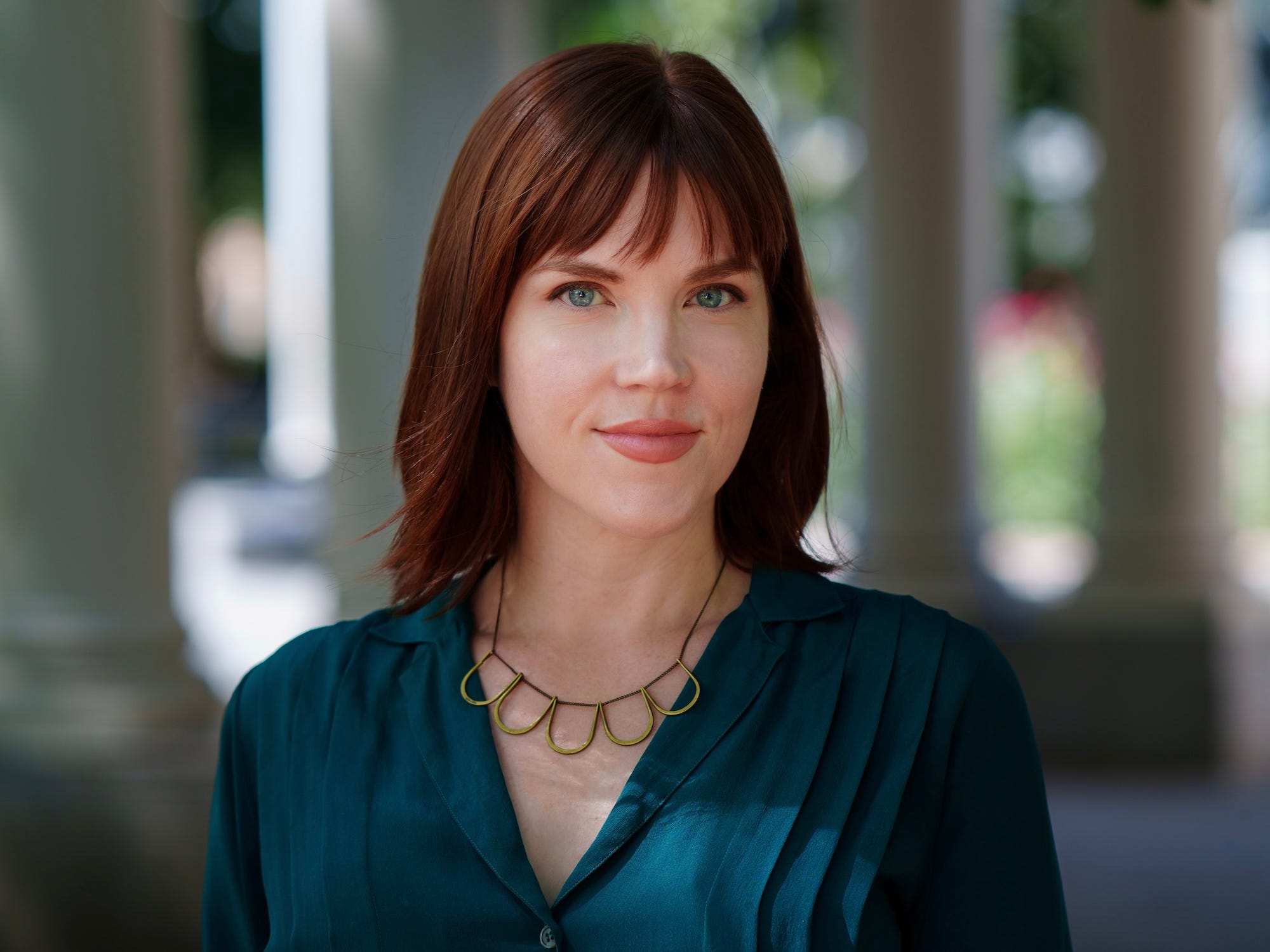 Melissa Riepe standing outdoor headshot wearing a green long-sleeve blouse and earthy patterned skirt.