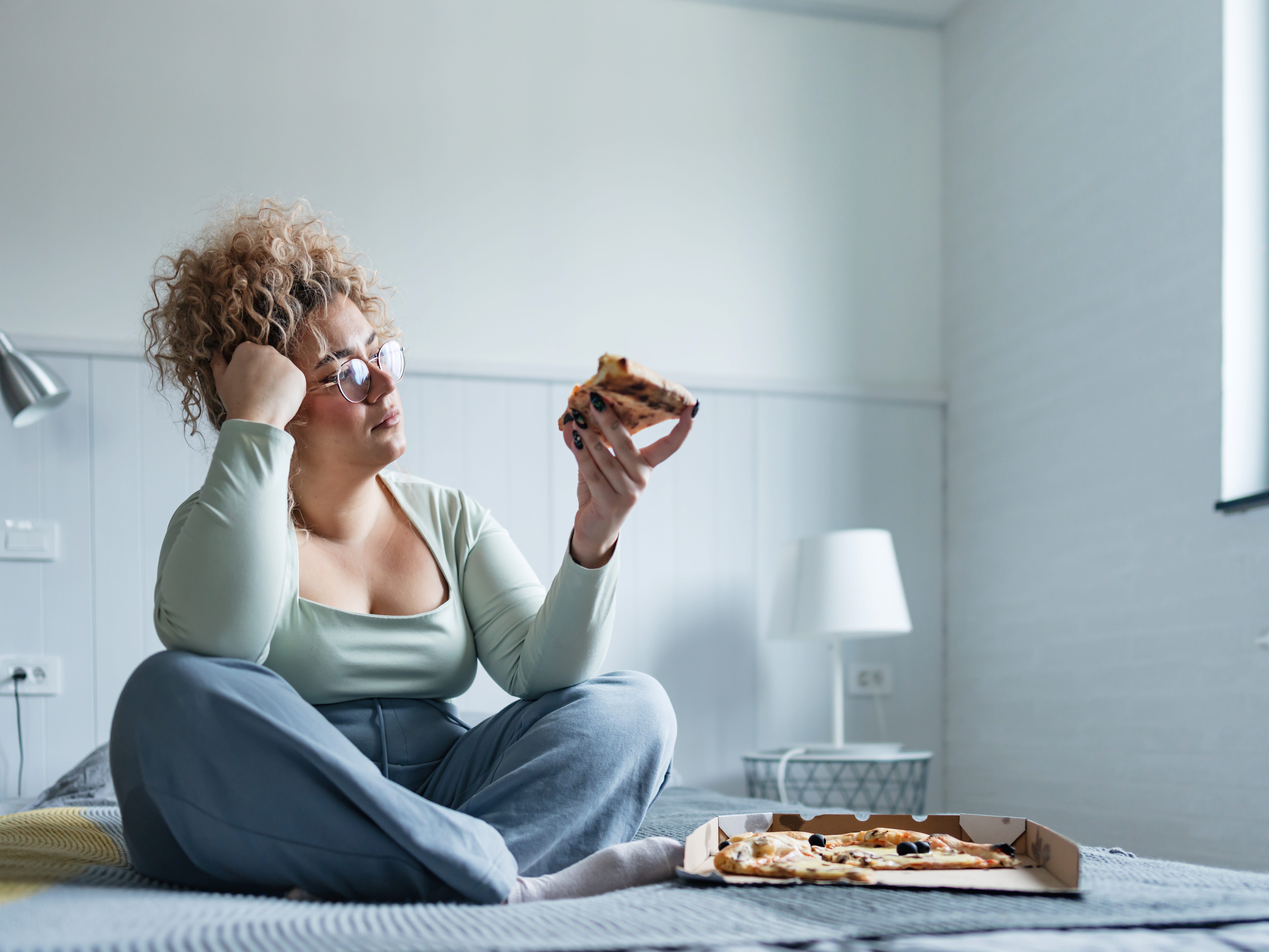 a lonely woman sitting in bed eat pizza