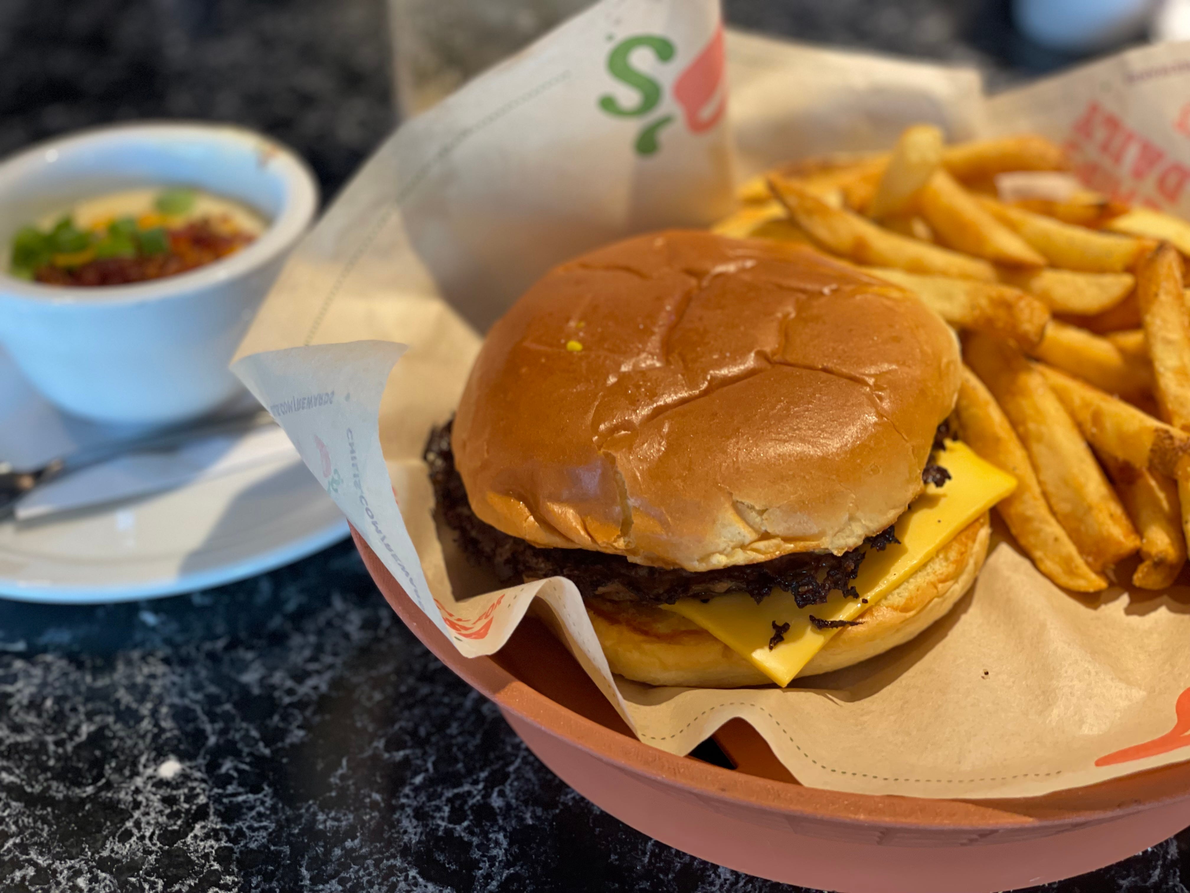 Burger with cheese served with fries on Chili's wax paper in basket with baked potato soup behind it