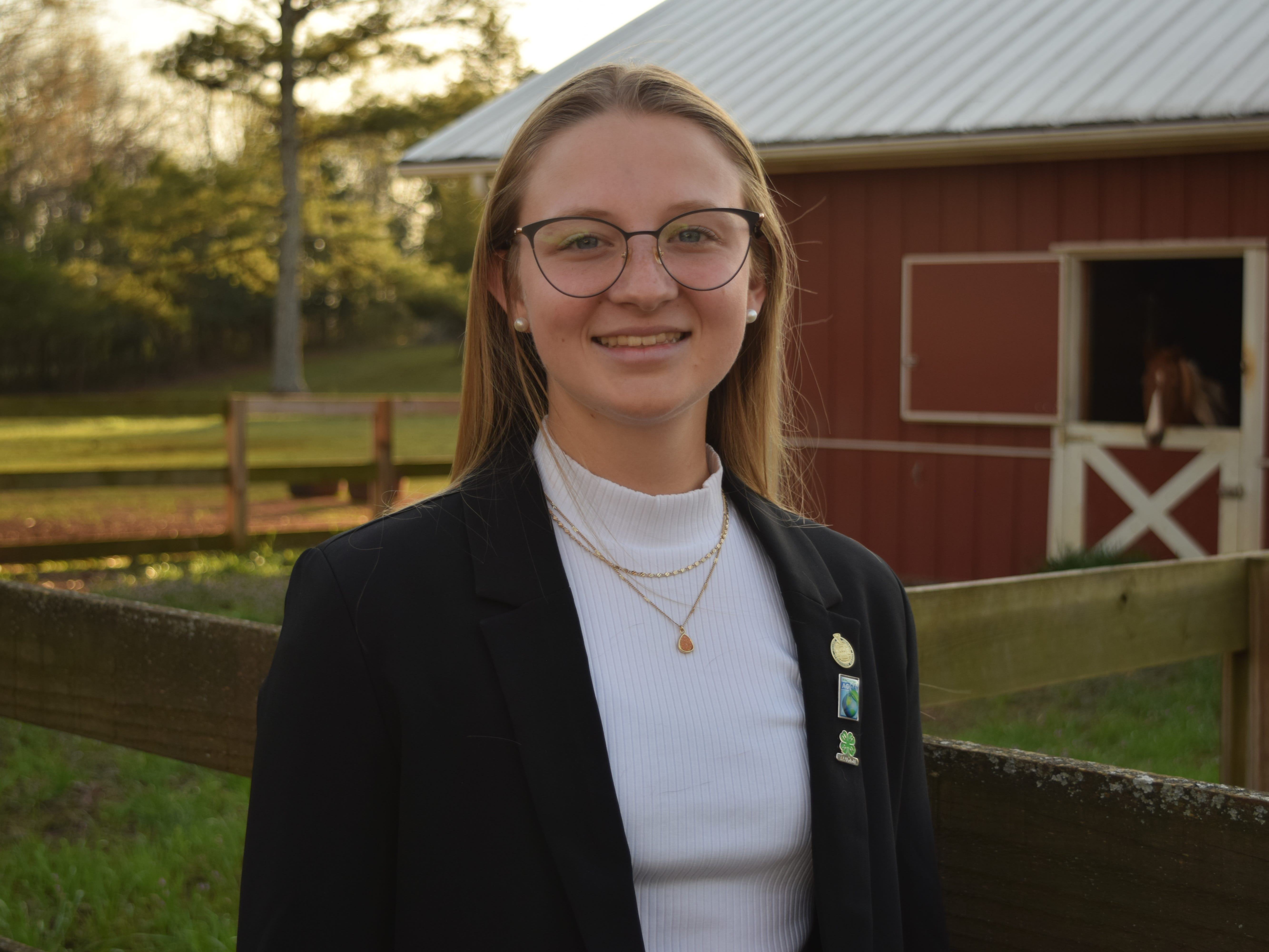 Emma Bayer in front of a barn with horses