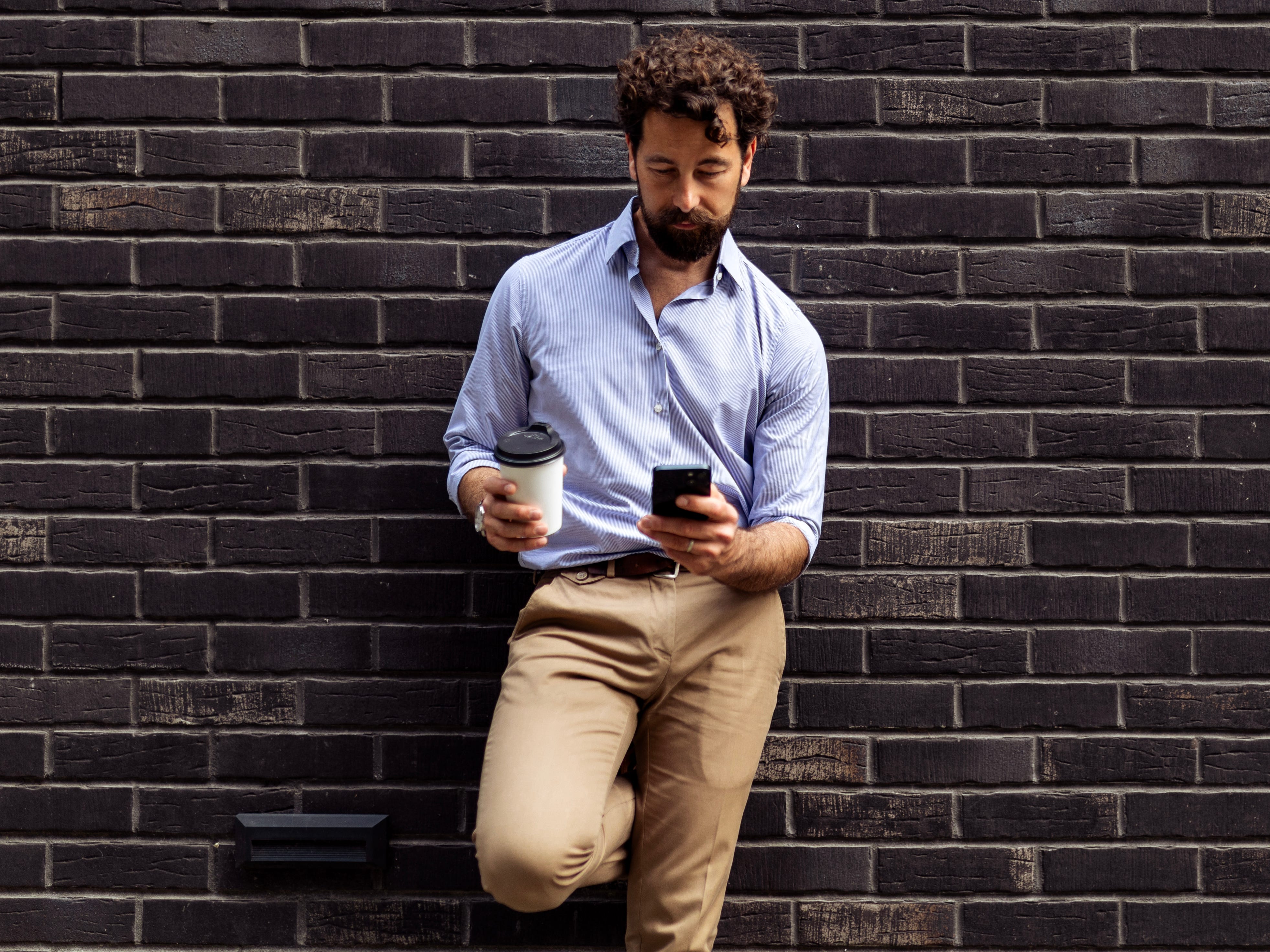 a man leaning against a wall and texting