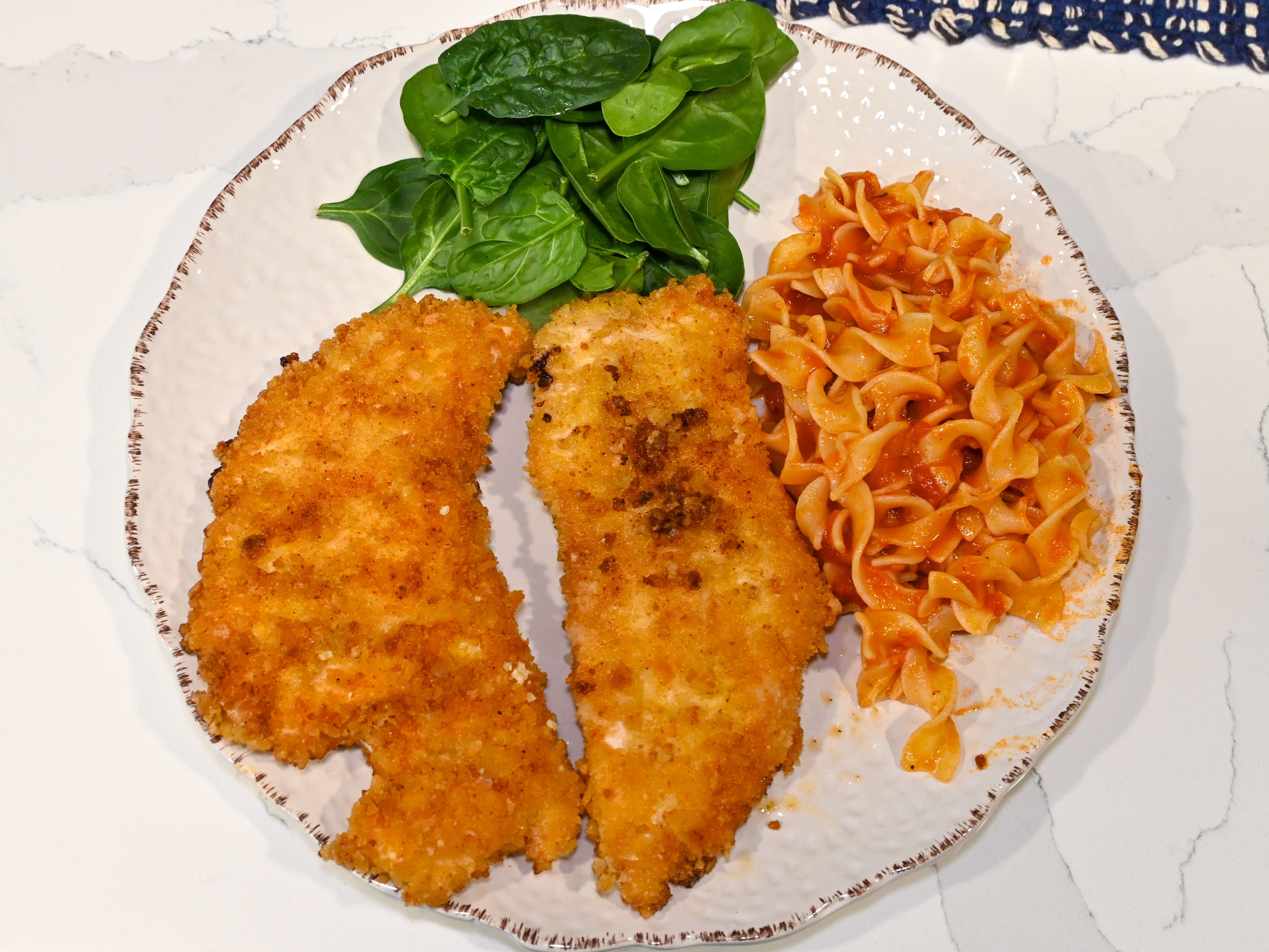 Two chicken cutlets arranged on a plate with pasta and spinach leaves.