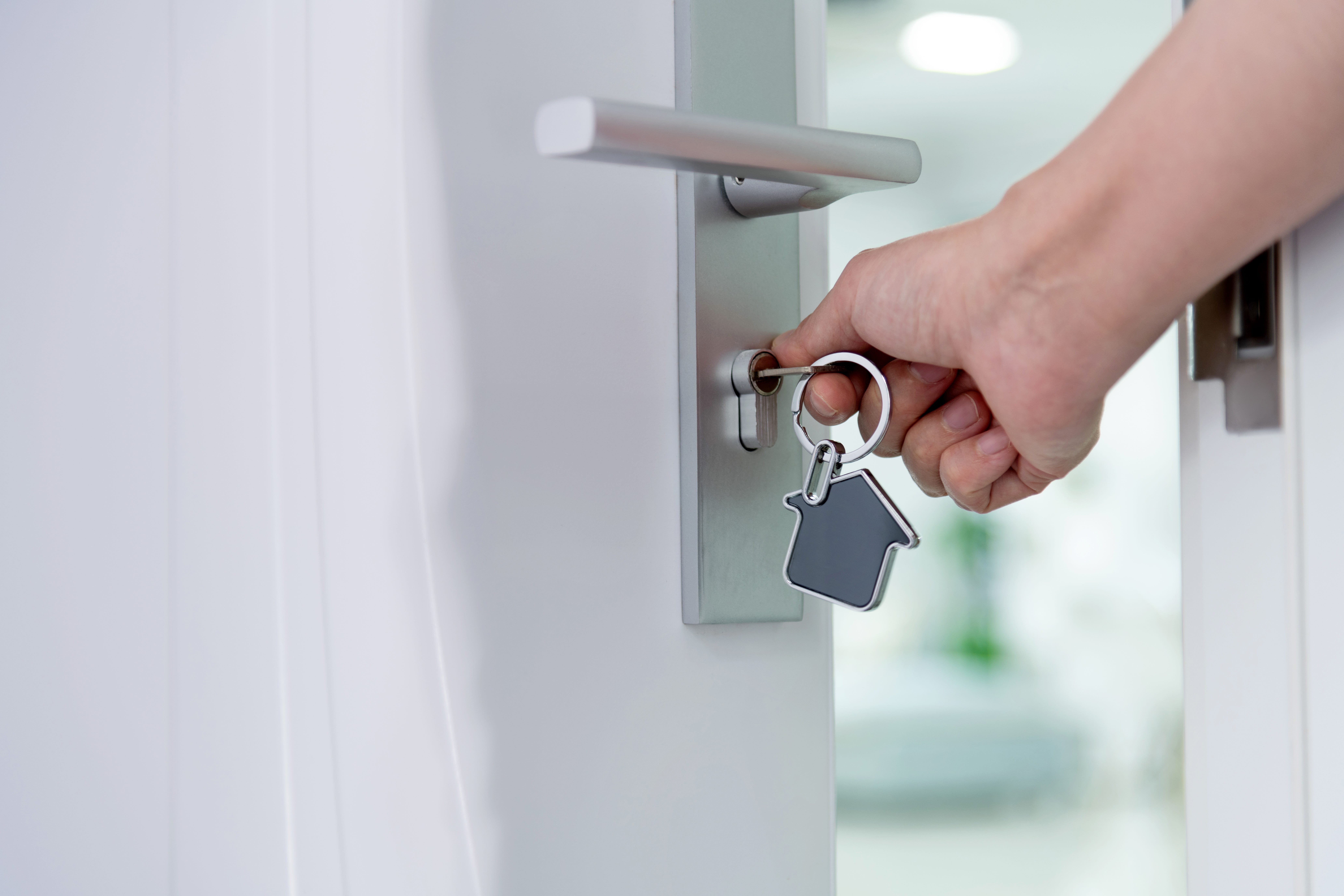 A hand opening a door with a key that has a house keychain.