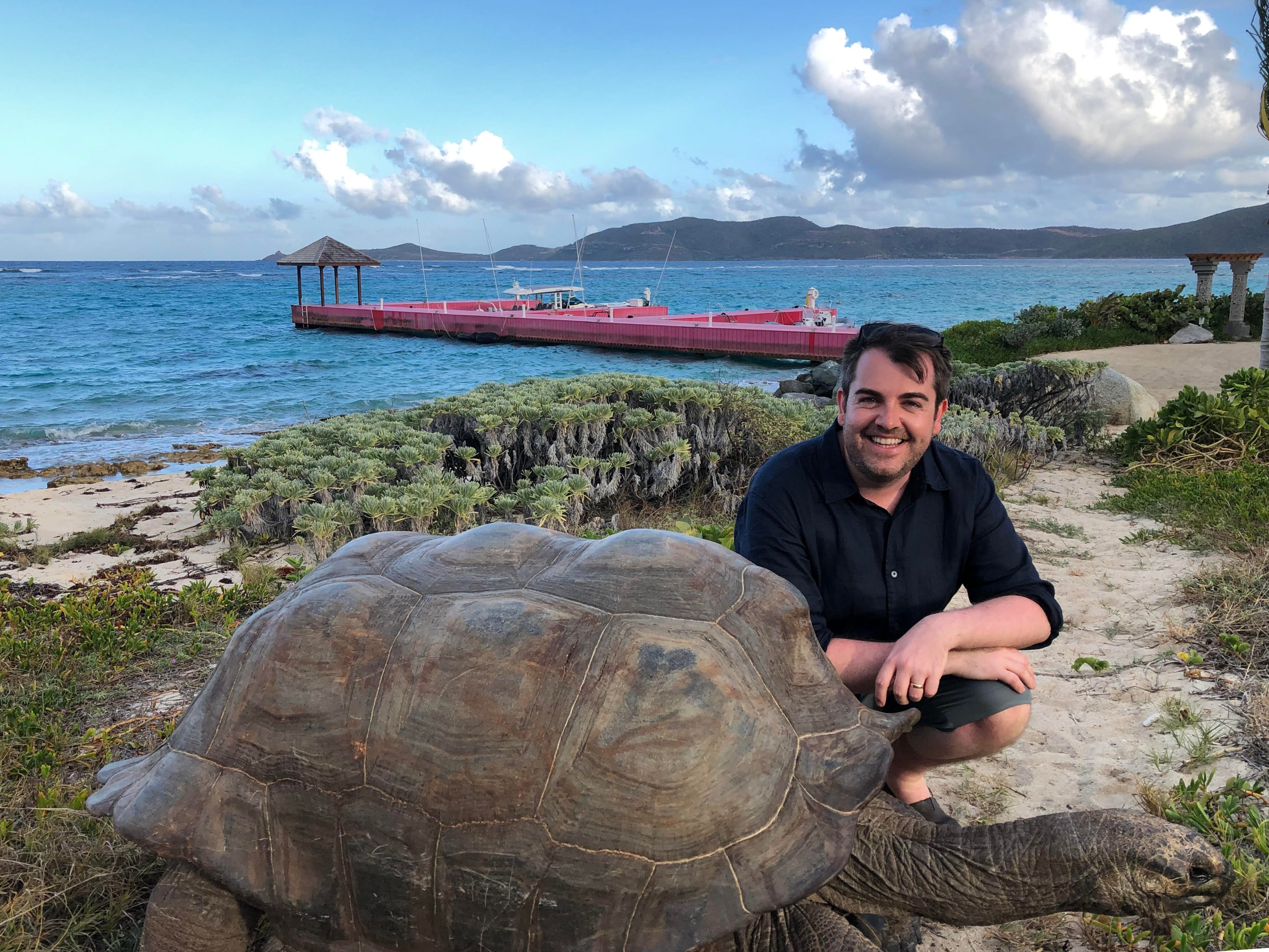A man crouches next to a tortoise in Necker Island.
